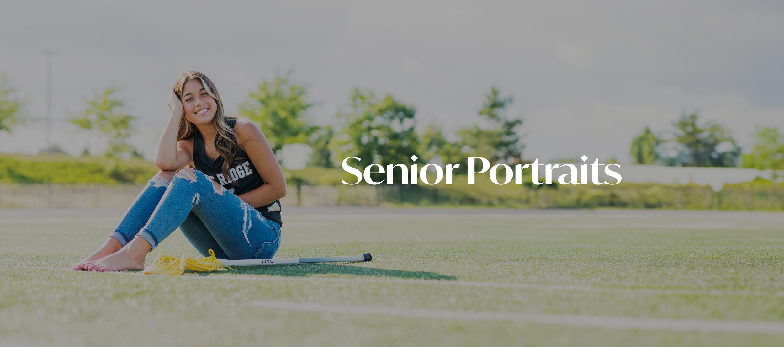 Young woman sitting on a field with a lacrosse stick, smiling, for senior portrait photography.