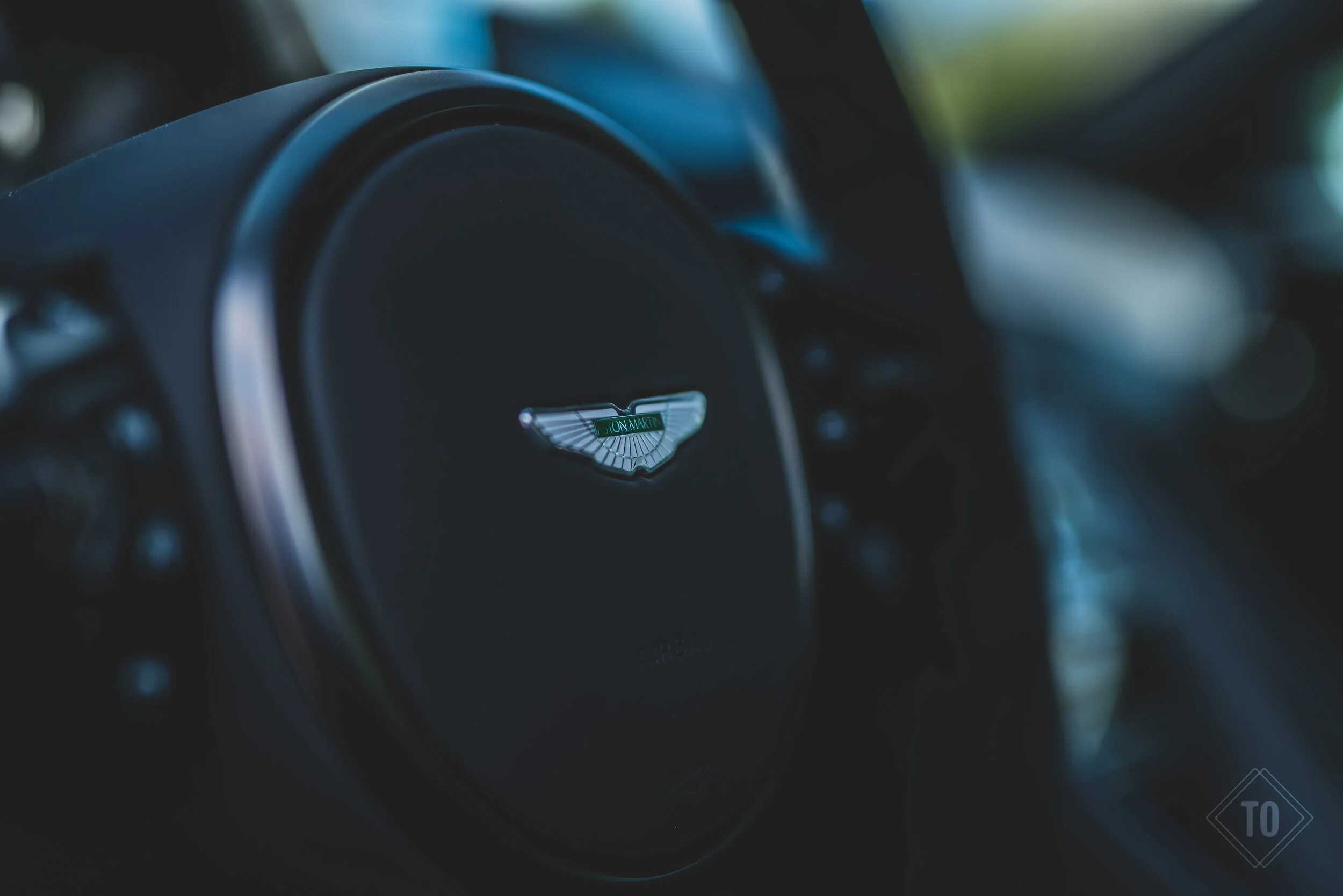 Close-up of a car steering wheel with the Aston Martin logo in the center.