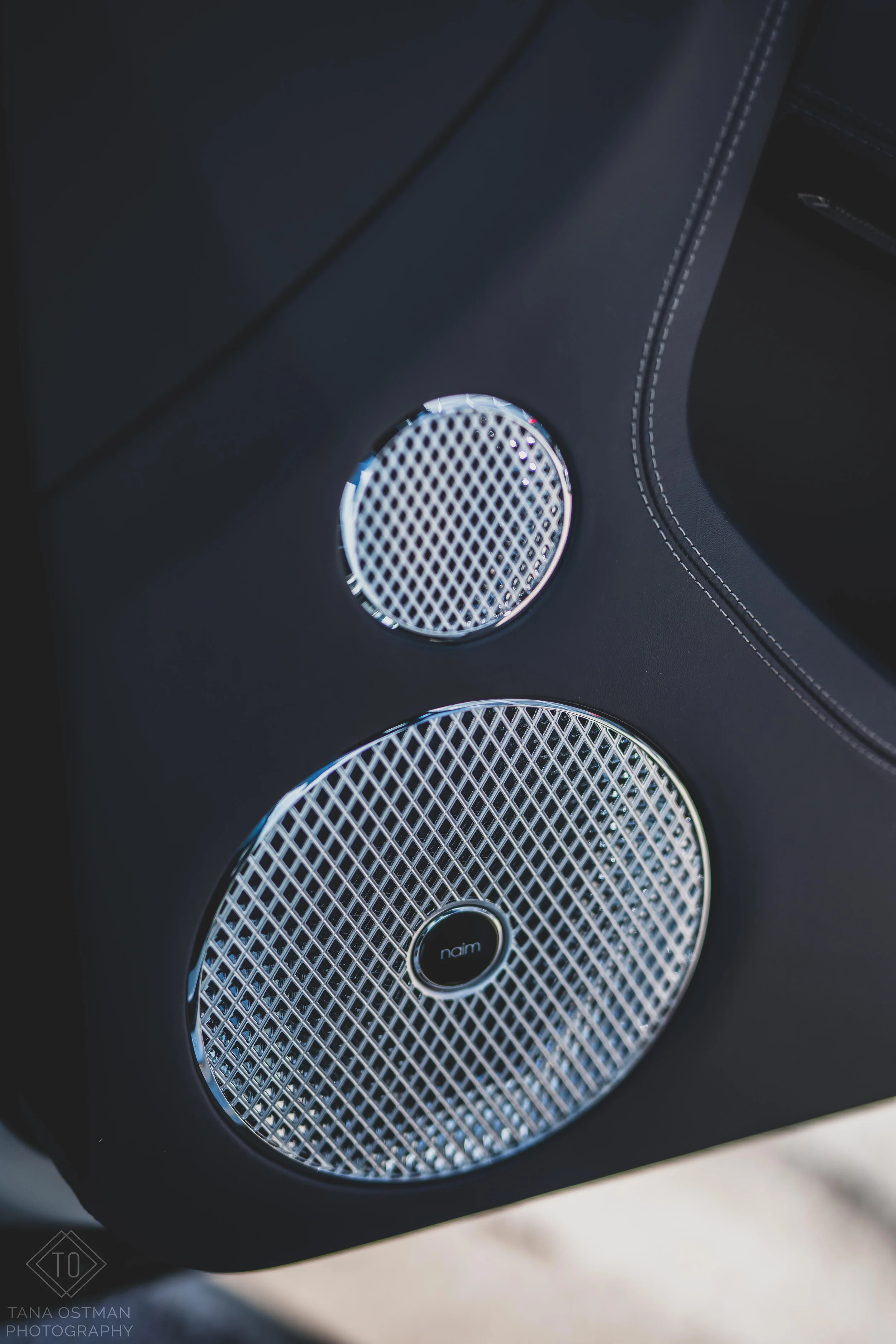Close-up of a black speaker system with two large silver speaker grilles, one above the other, on a dark surface.