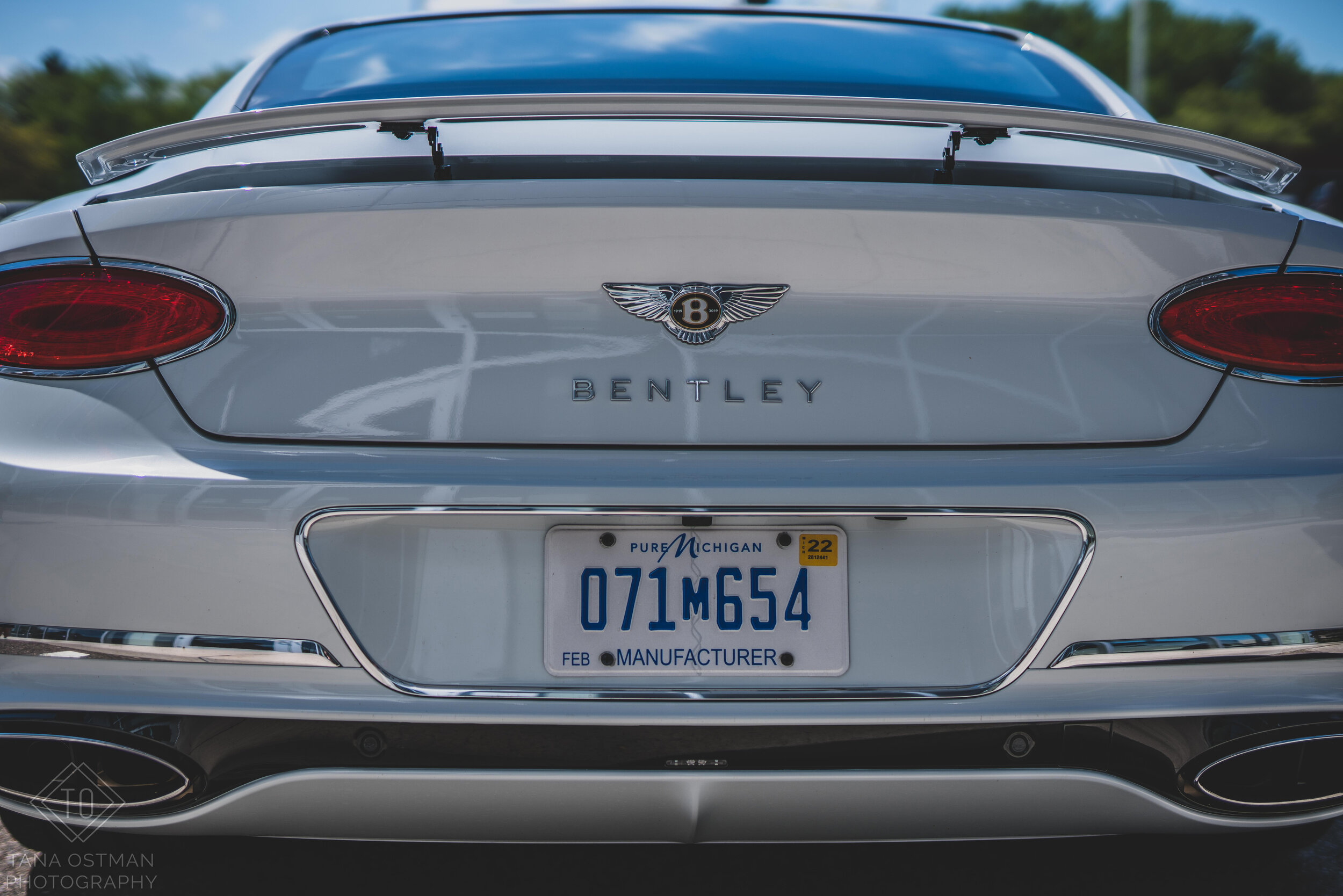The rear view of a silver Bentley convertible car with a Michigan license plate, Bentley logo, and model badge.