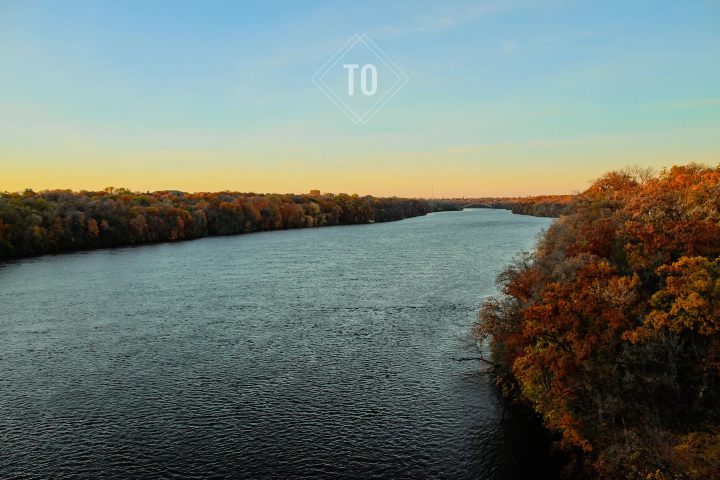 A river flowing through a landscape with colorful autumn trees on both sides, under a clear sky, with the word 'TO' overlaid at the top.