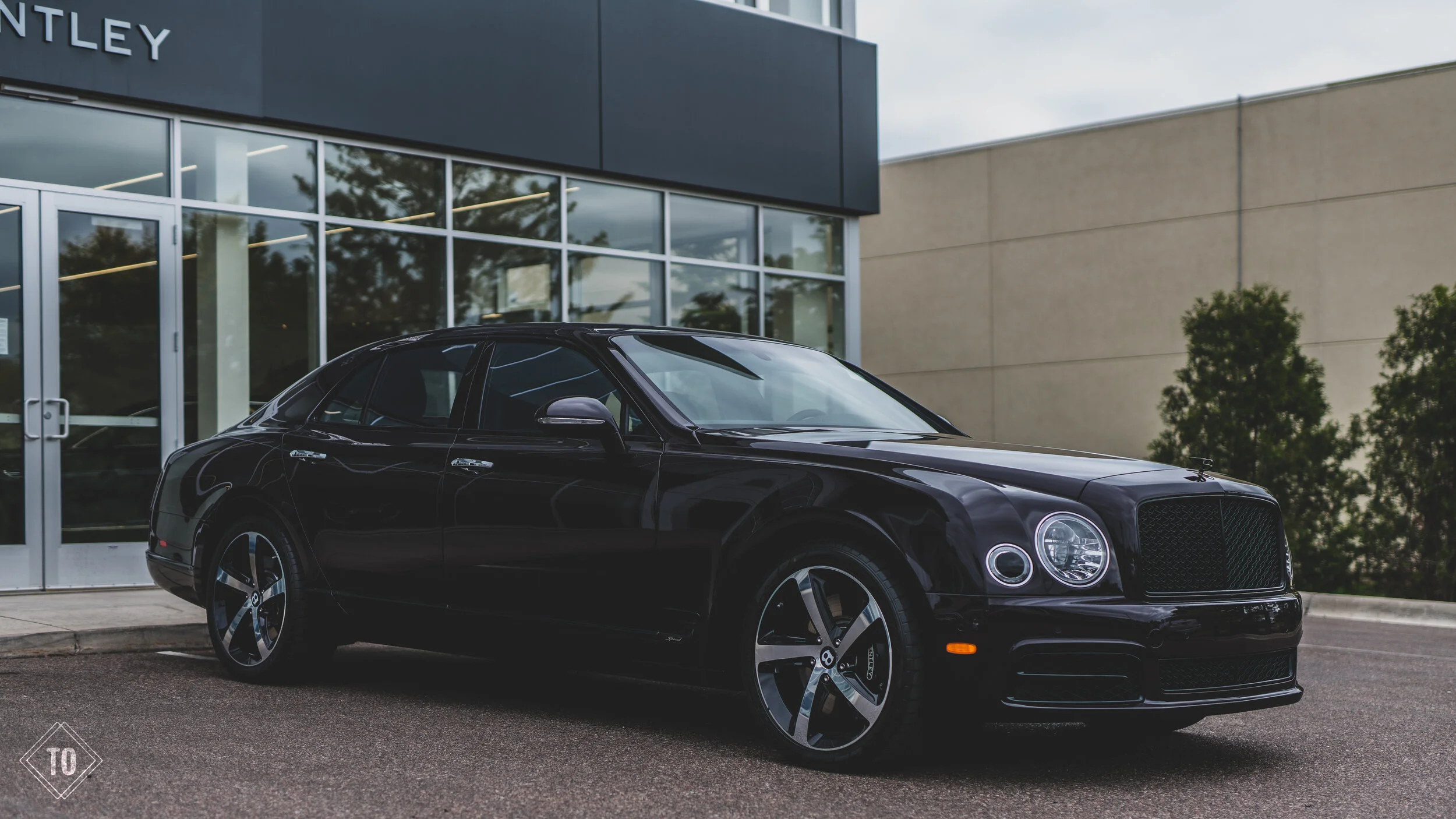 A black luxury sedan parked outside a modern car dealership with large glass windows.