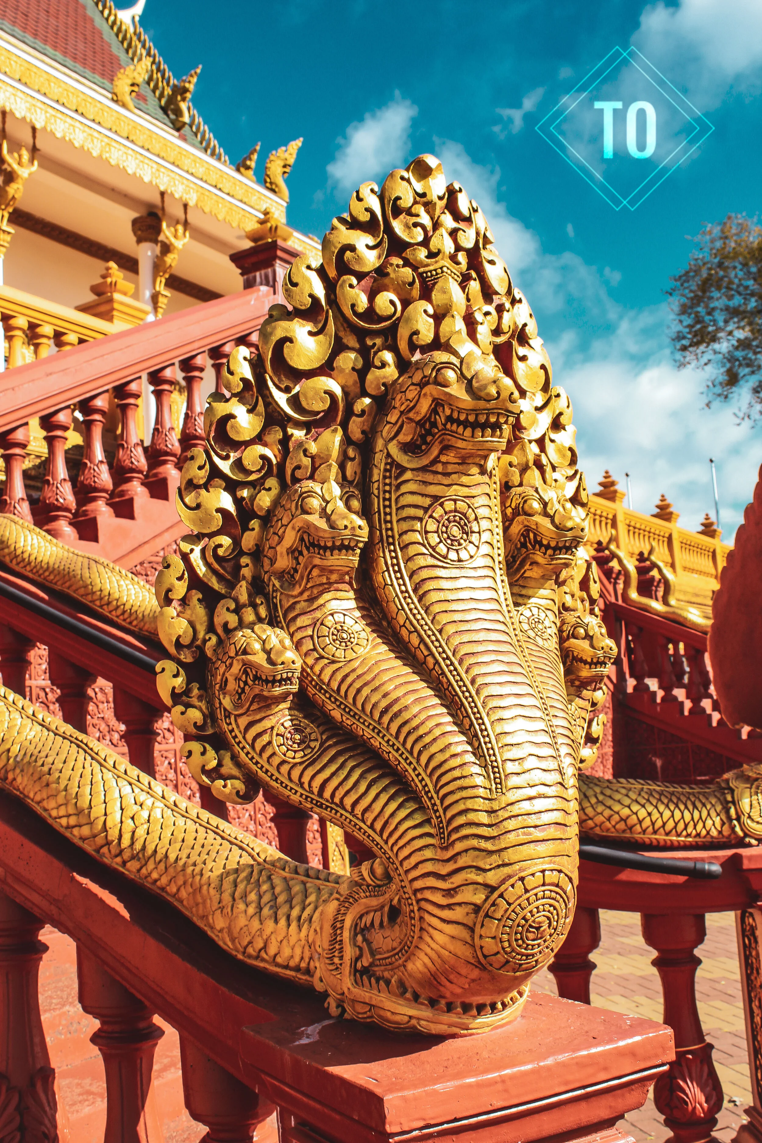 Golden serpentine sculpture with multiple heads, part of traditional Asian temple architecture, with a colorful sky and temple structure in the background.
