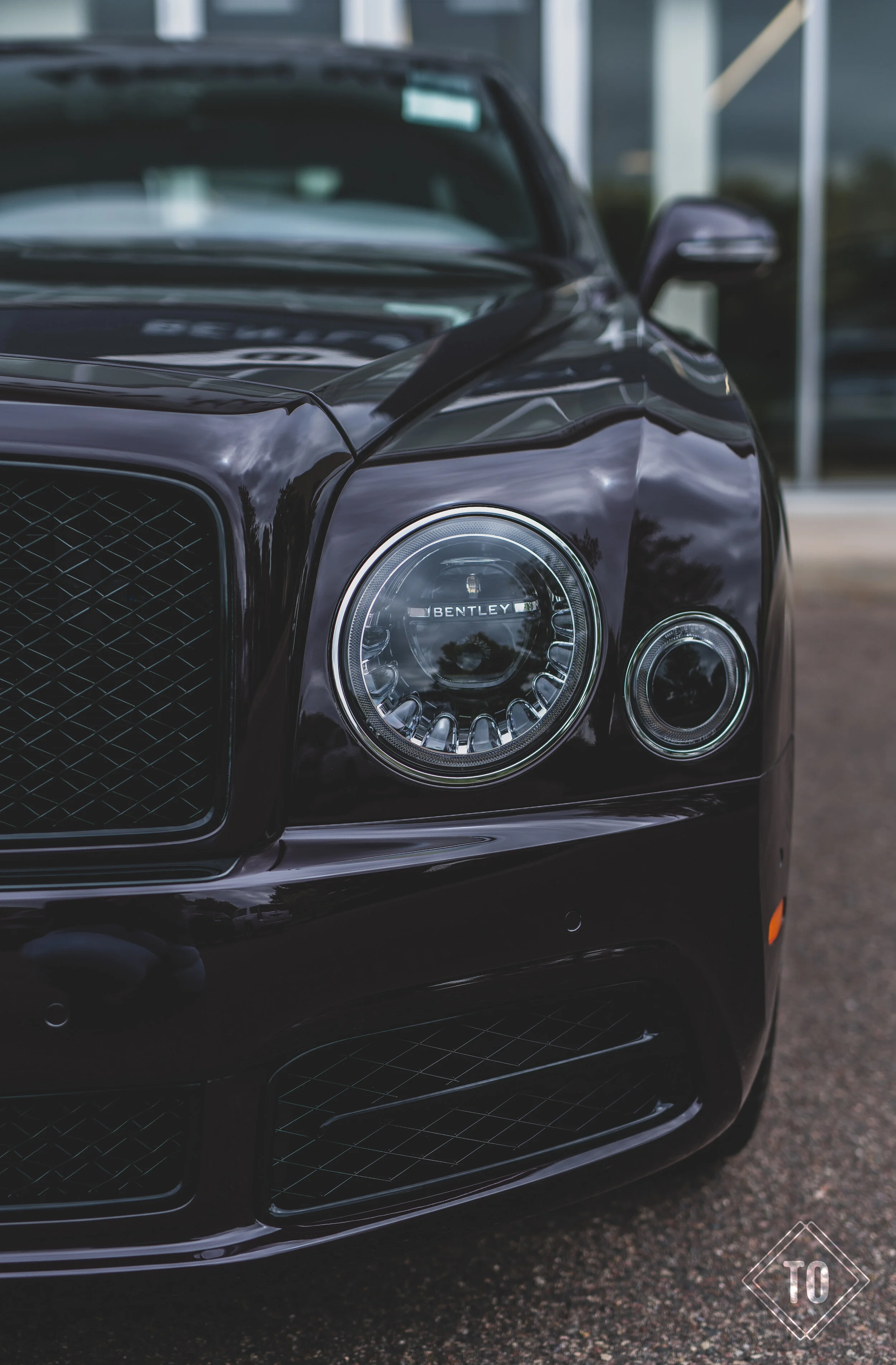 Close-up of the front right headlight of a black Bentley car parked outside.
