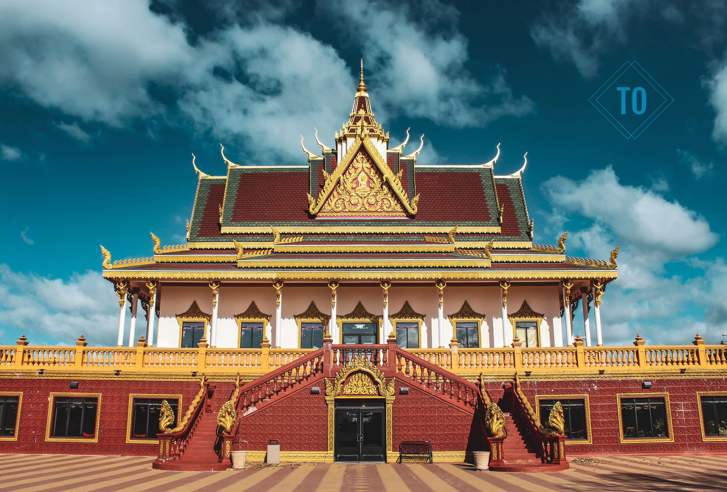 Traditional Thai temple with ornate golden trim, multiple rooftops, and a staircase leading to the entrance, set against a partly cloudy sky.