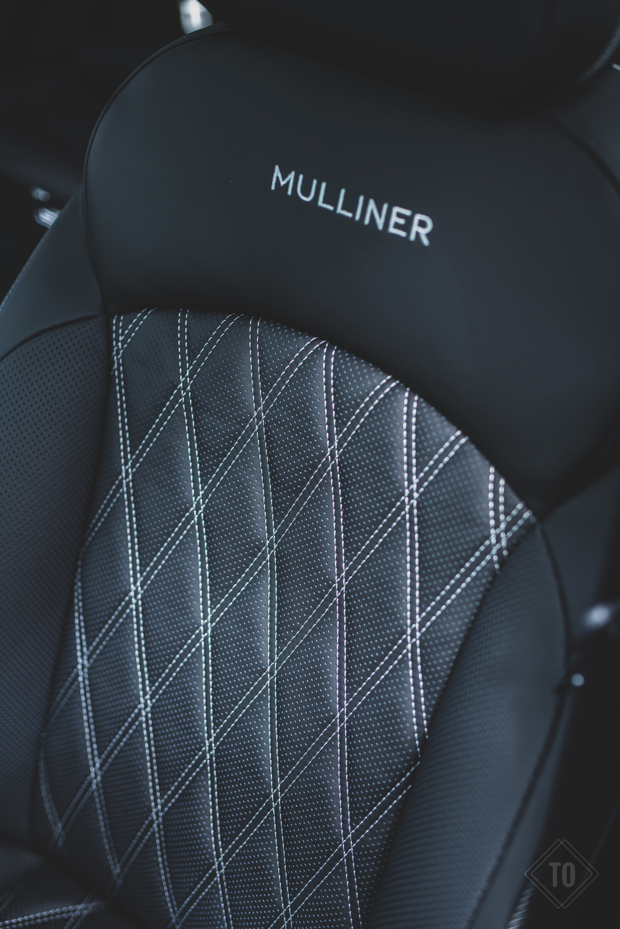 Close-up of a black luxury car seat with diamond quilted stitching and the word 'MULLINER' embroidered on the headrest.