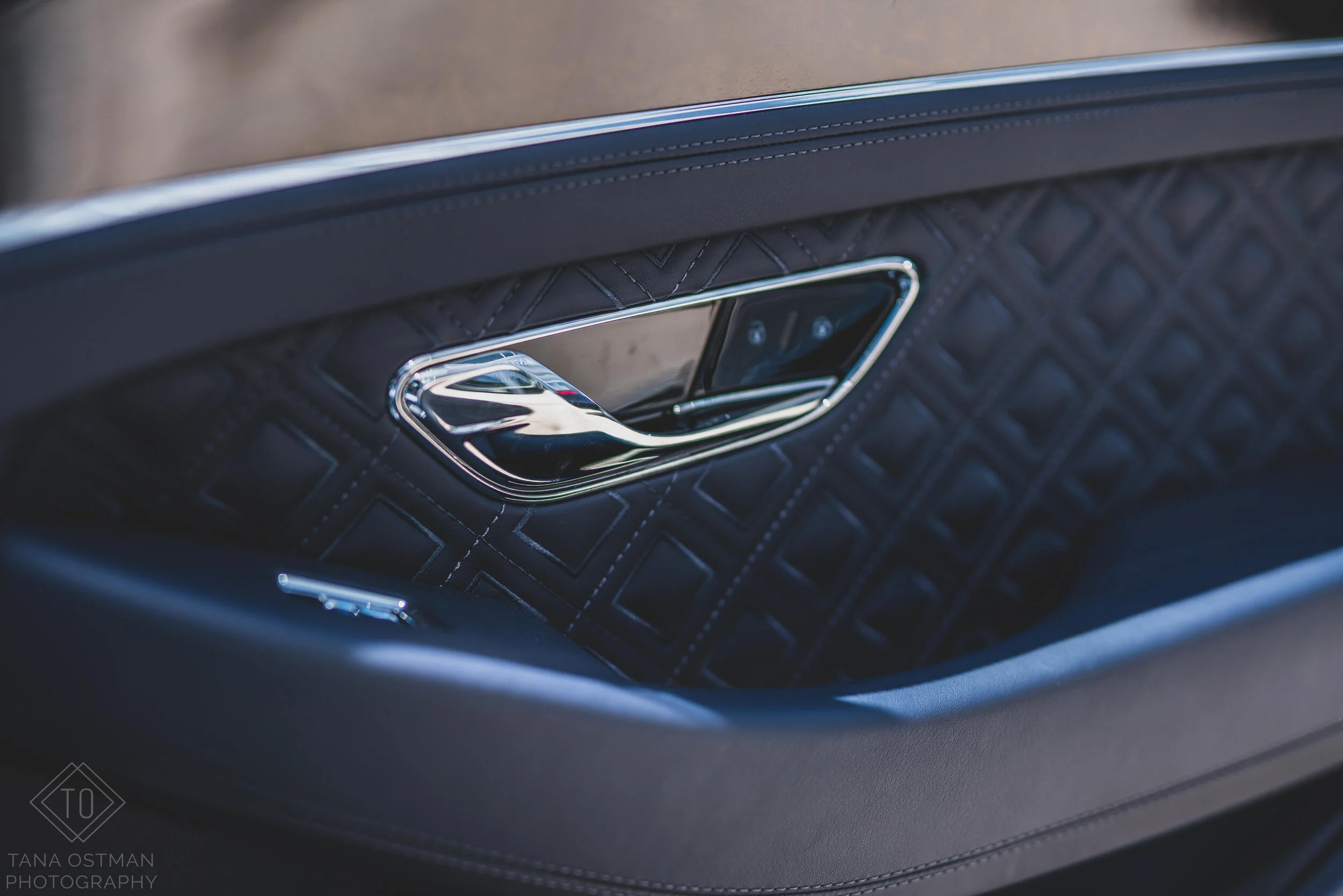 Close-up of a car door handle with a reflective chrome finish, set against a black quilted interior panel.