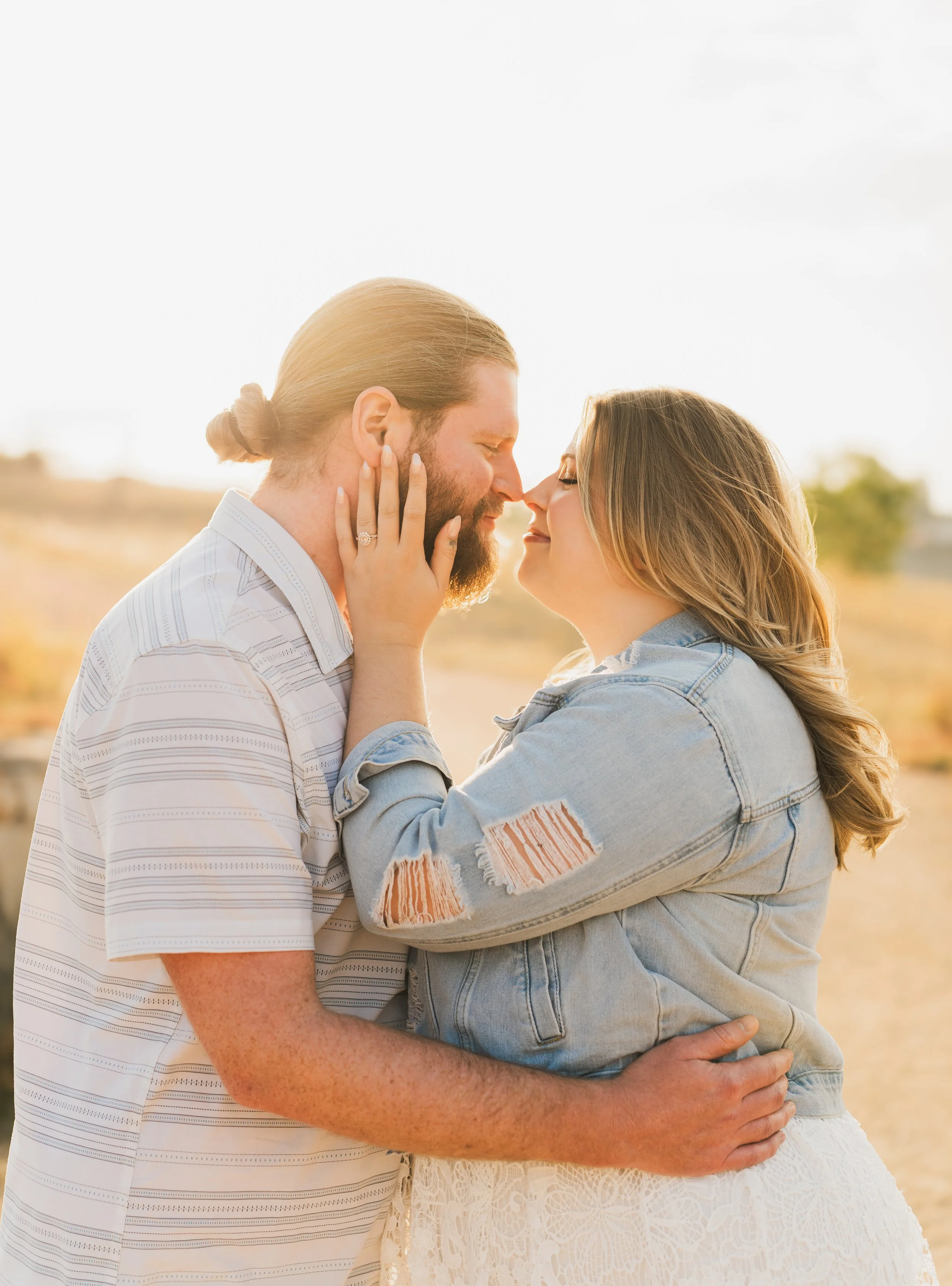 A couple loving embrace outdoors, touching noses, with a blurred landscape background