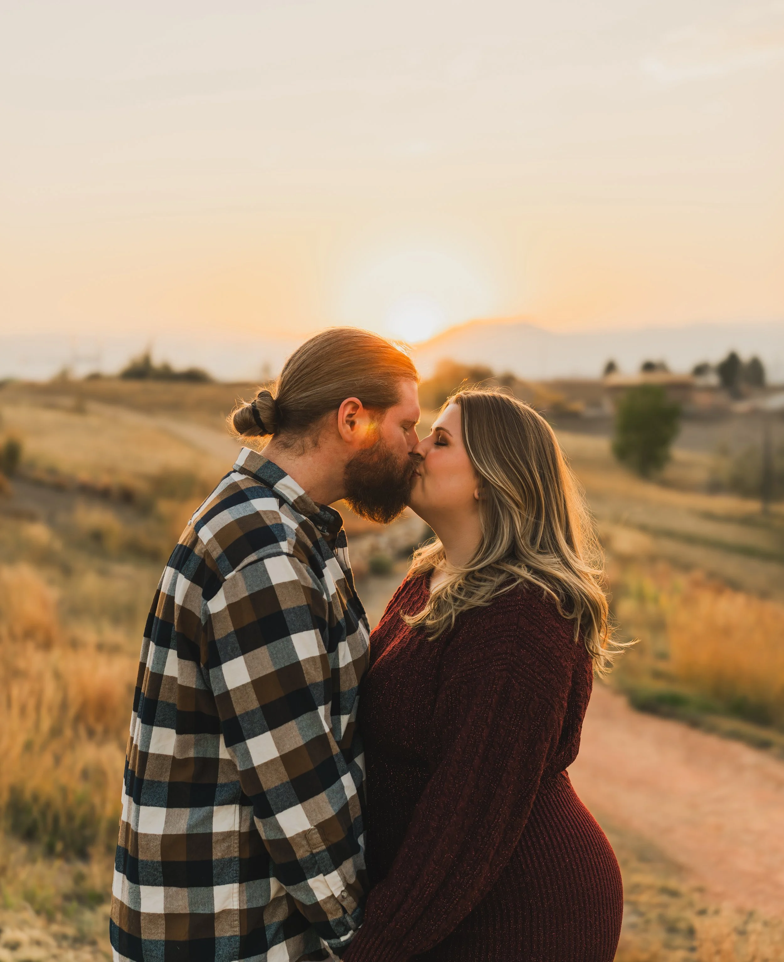 A couple sharing a kiss during sunset in a scenic outdoor setting.