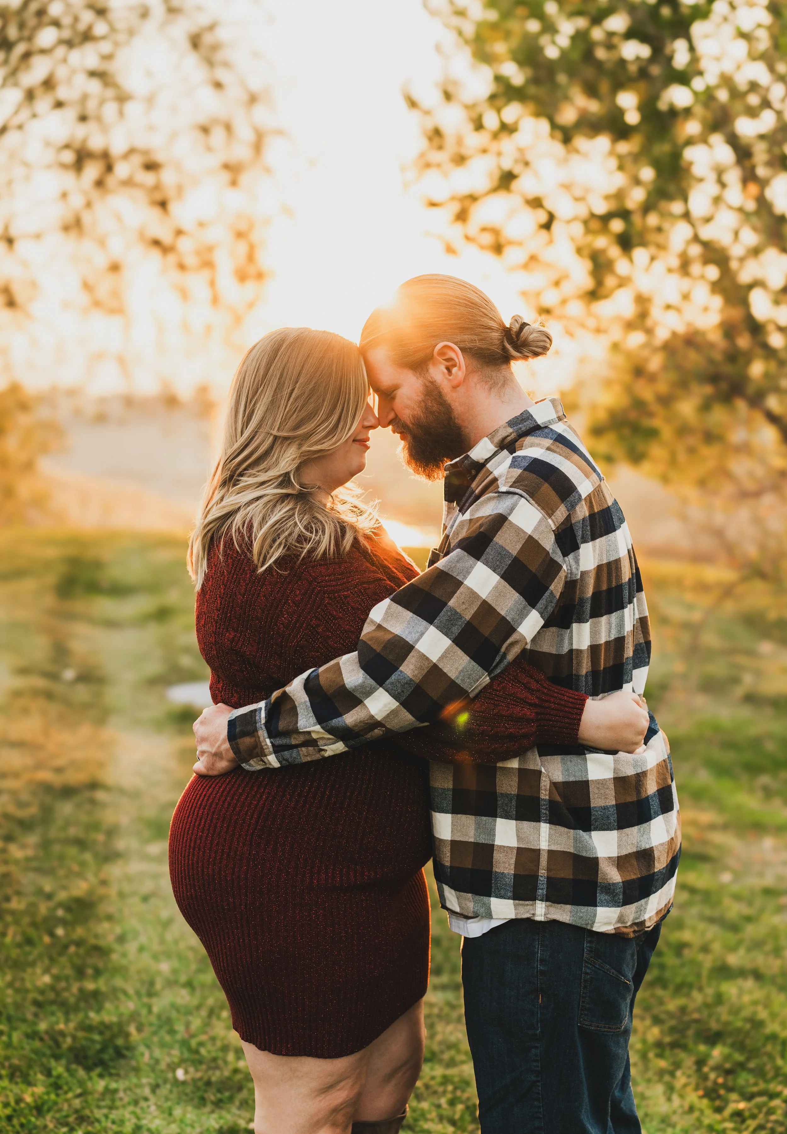 A couple embracing during sunset in a park with trees and green grass.
