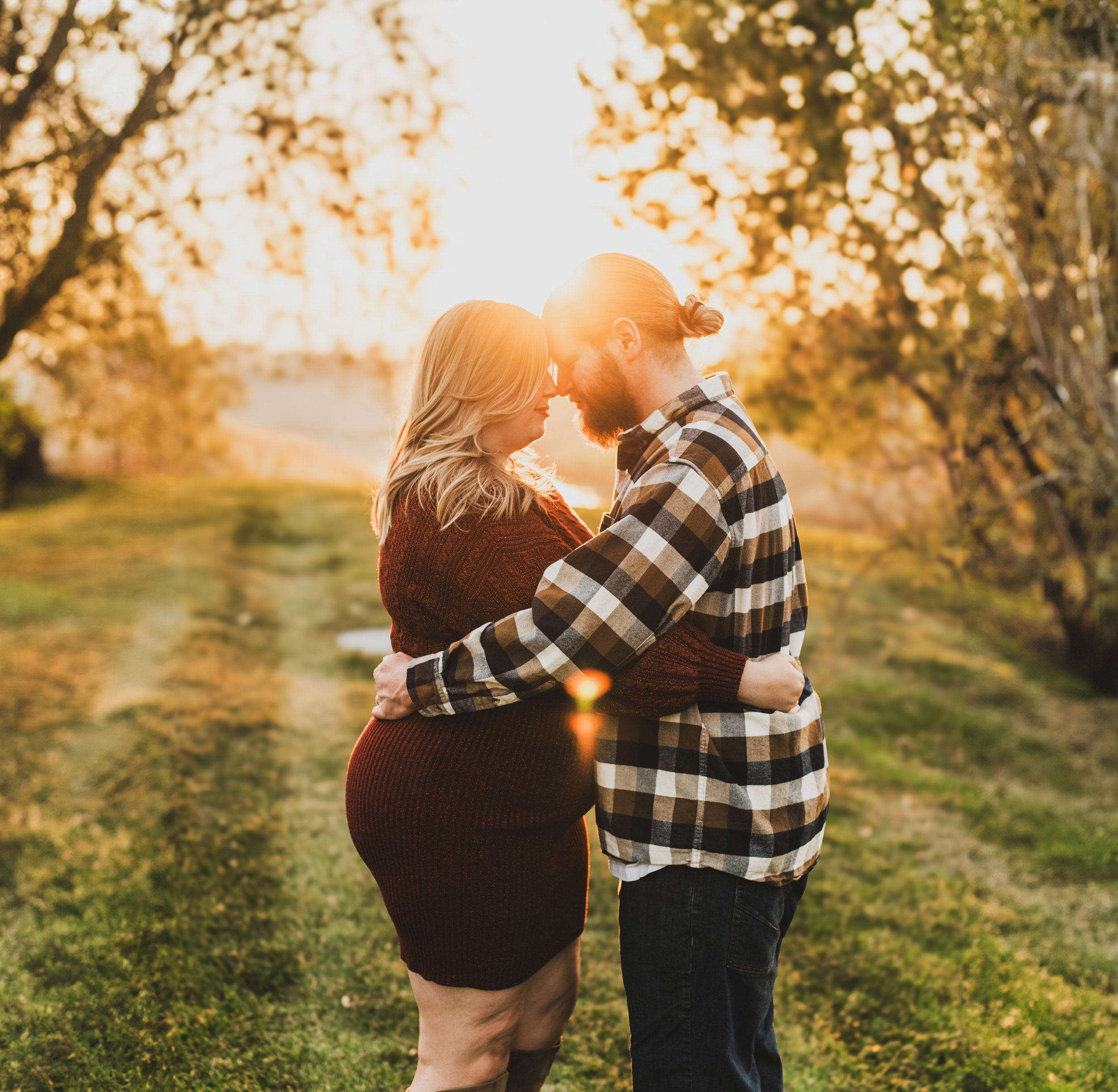 A couple embracing outdoors at sunset amid trees with golden leaves.