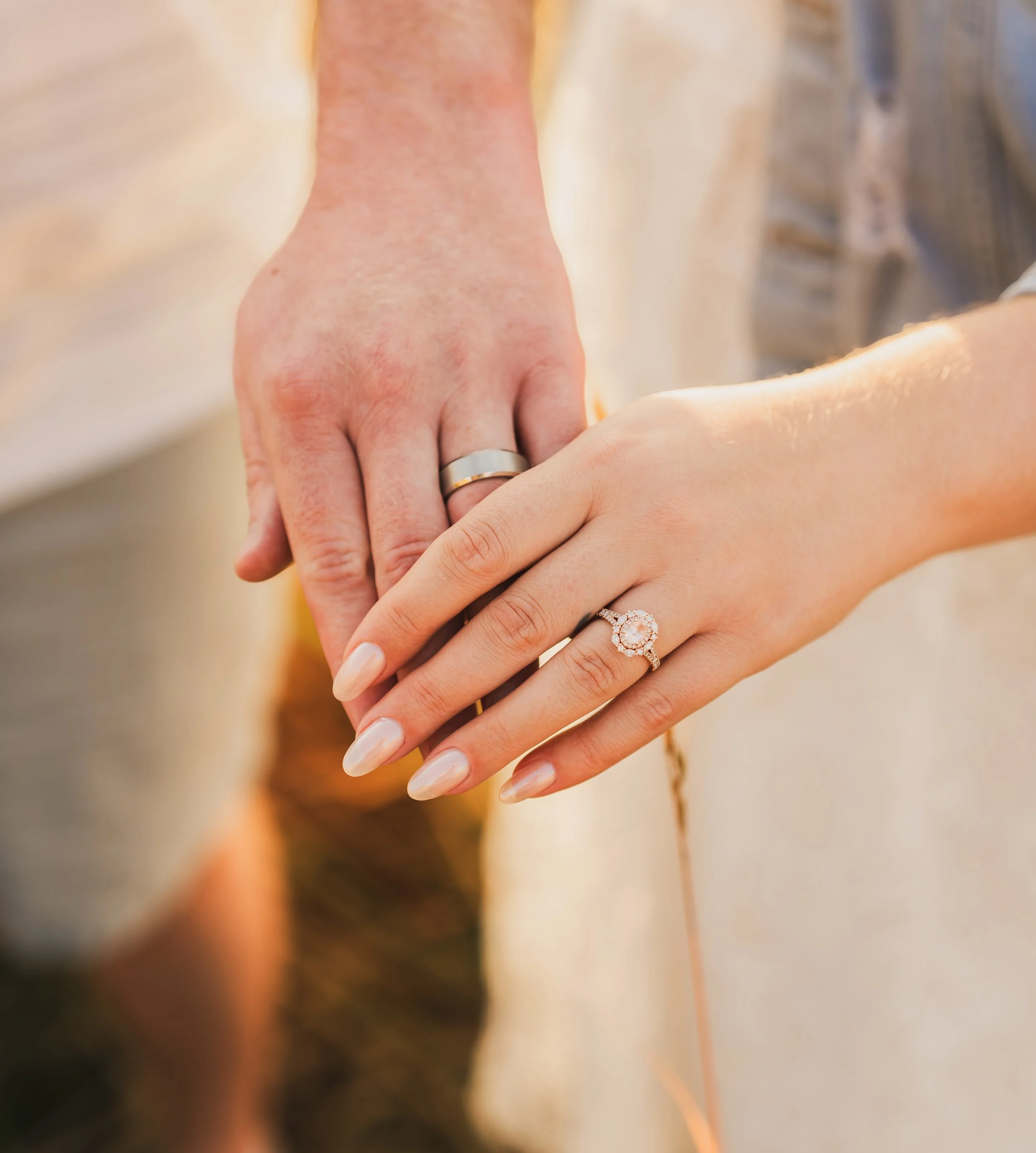 Close-up of a bride and groom holding hands, showing wedding rings and a diamond engagement ring on the bride's hand.