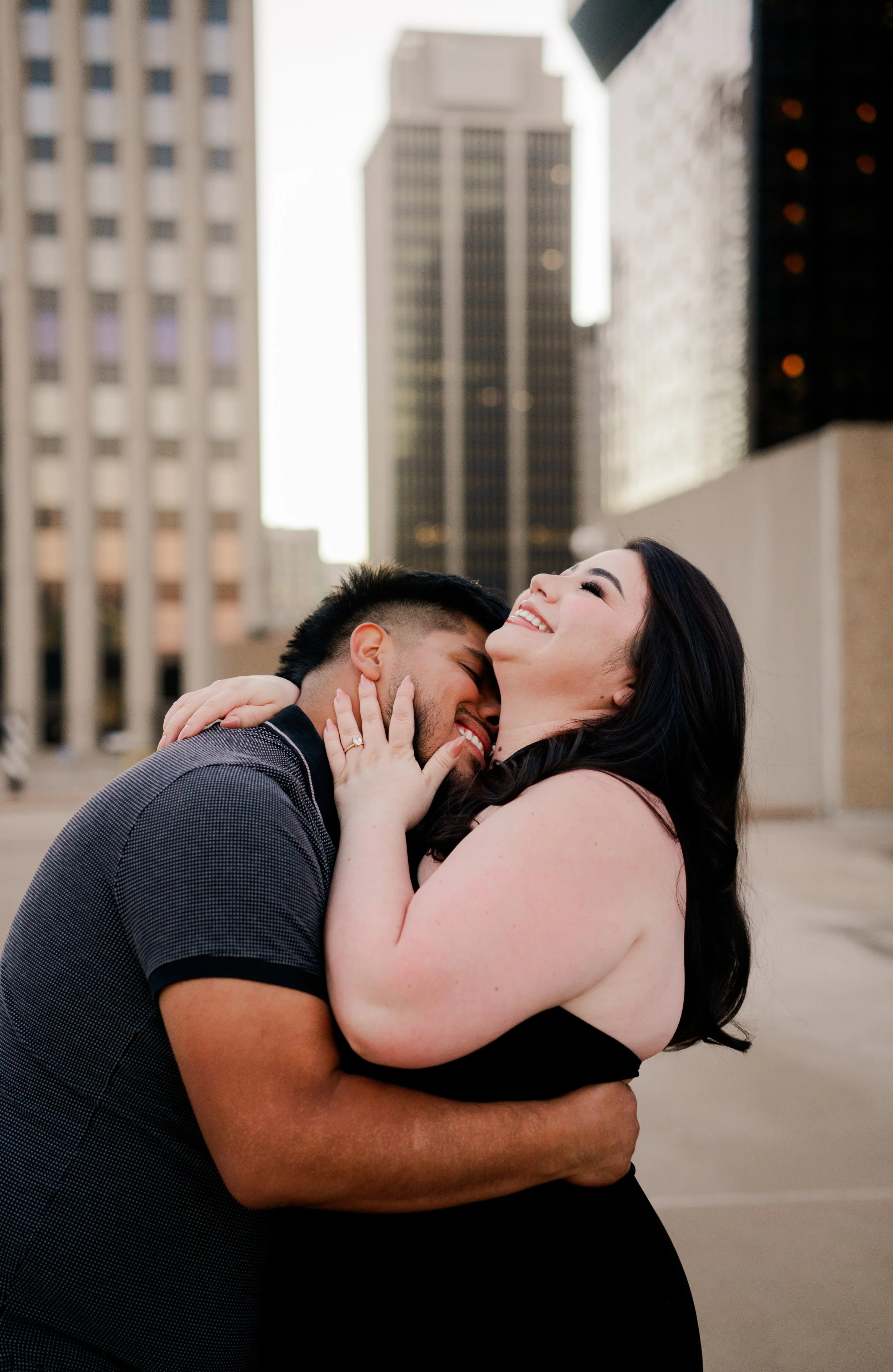 A happy couple embraces on a city rooftop with tall buildings in the background.