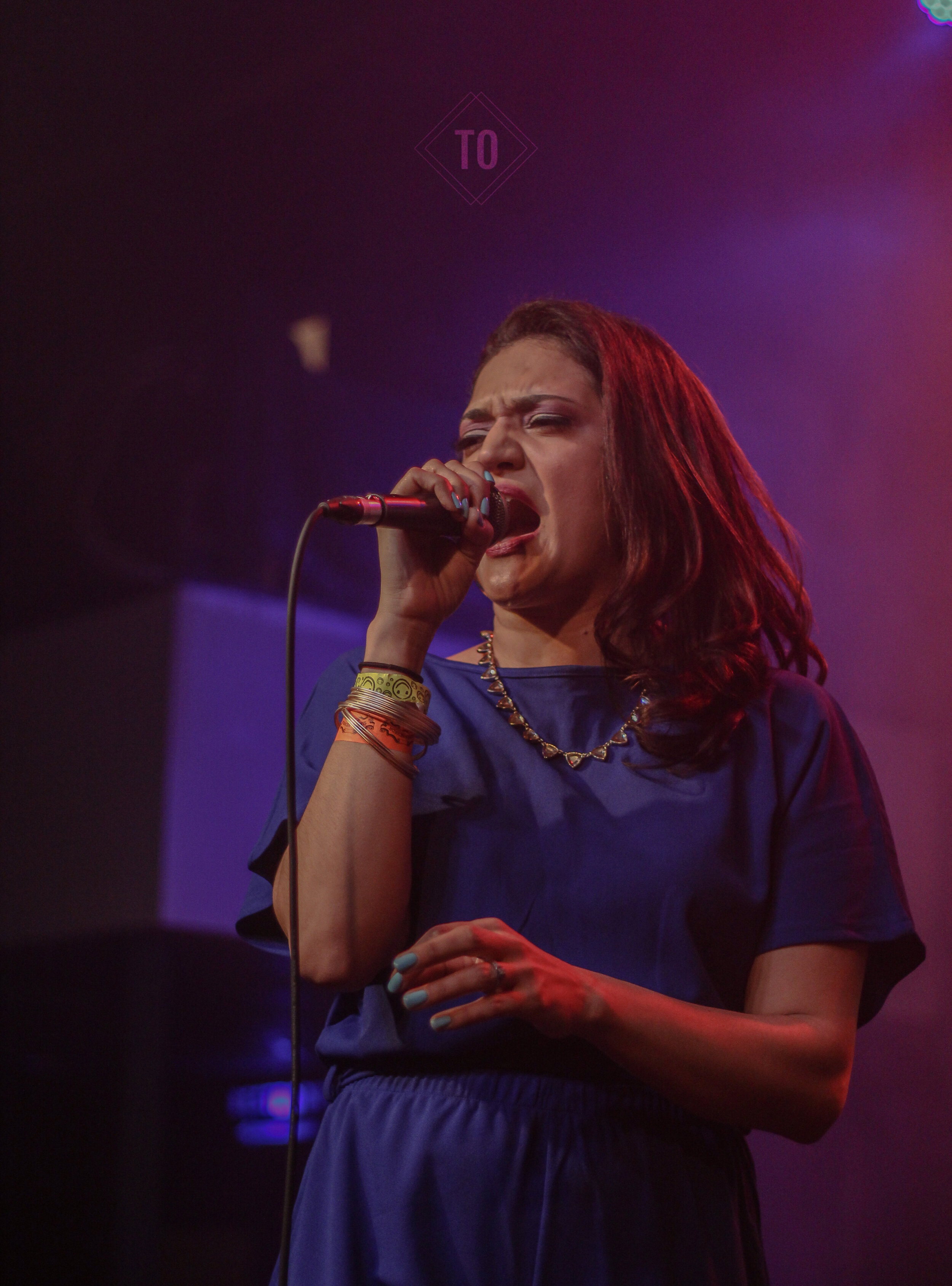 A woman singing passionately into a microphone on stage, with purple and red stage lighting.