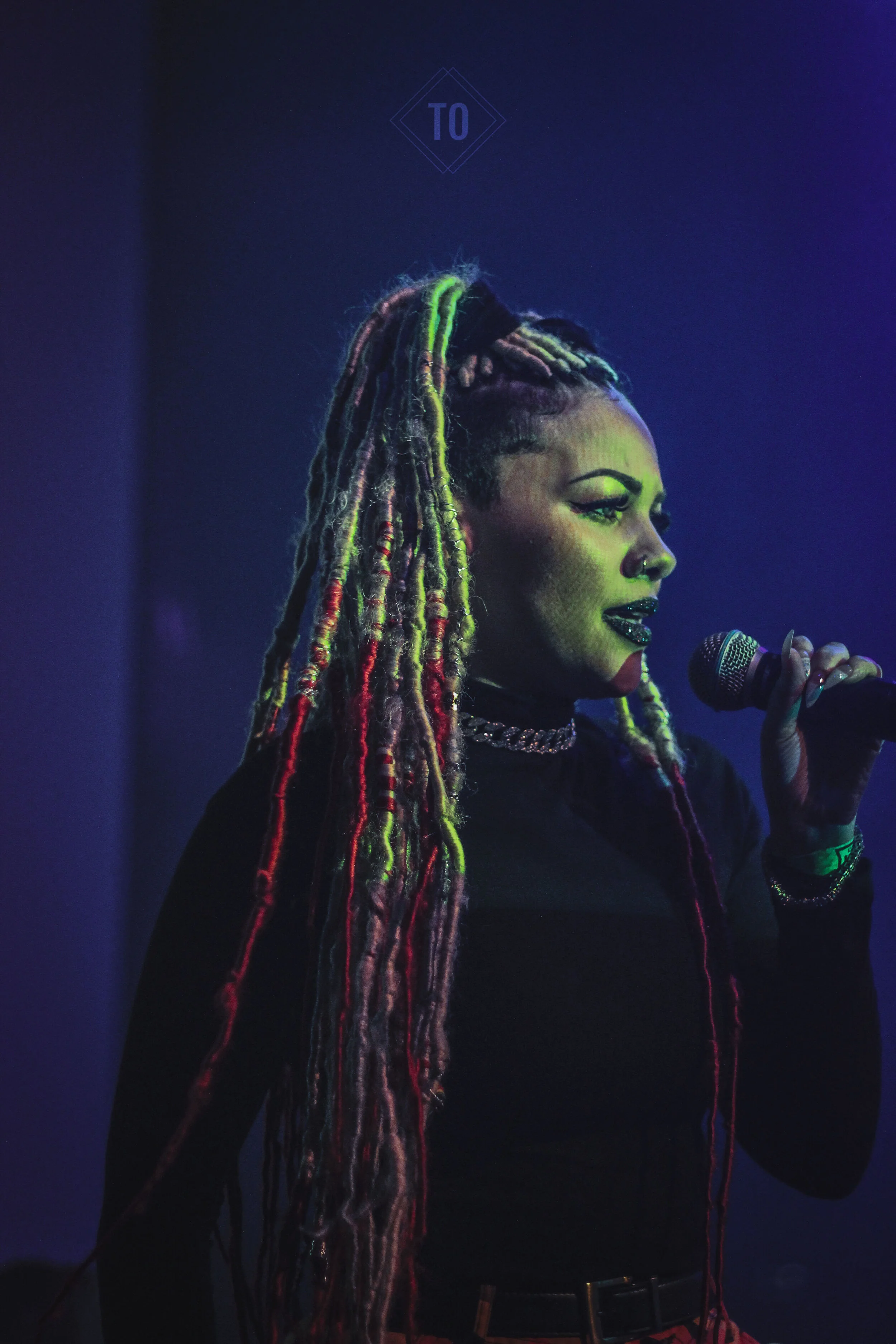 A woman with long, colorful dreadlocks holding a microphone on stage.