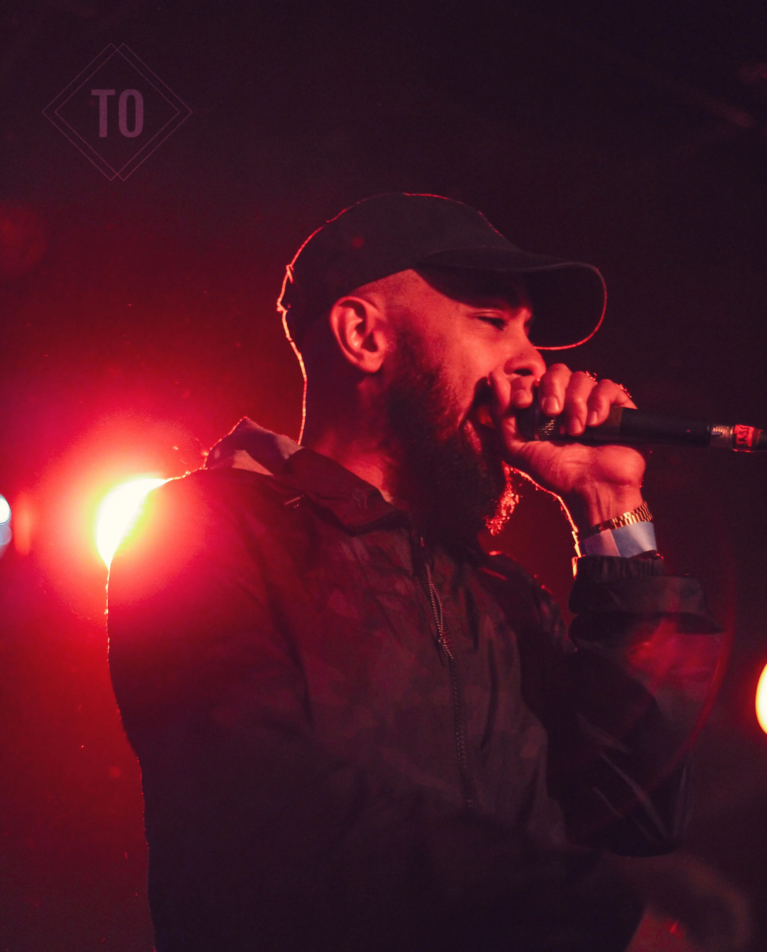 A man singing into a microphone on stage, backlit with red and orange stage lighting.