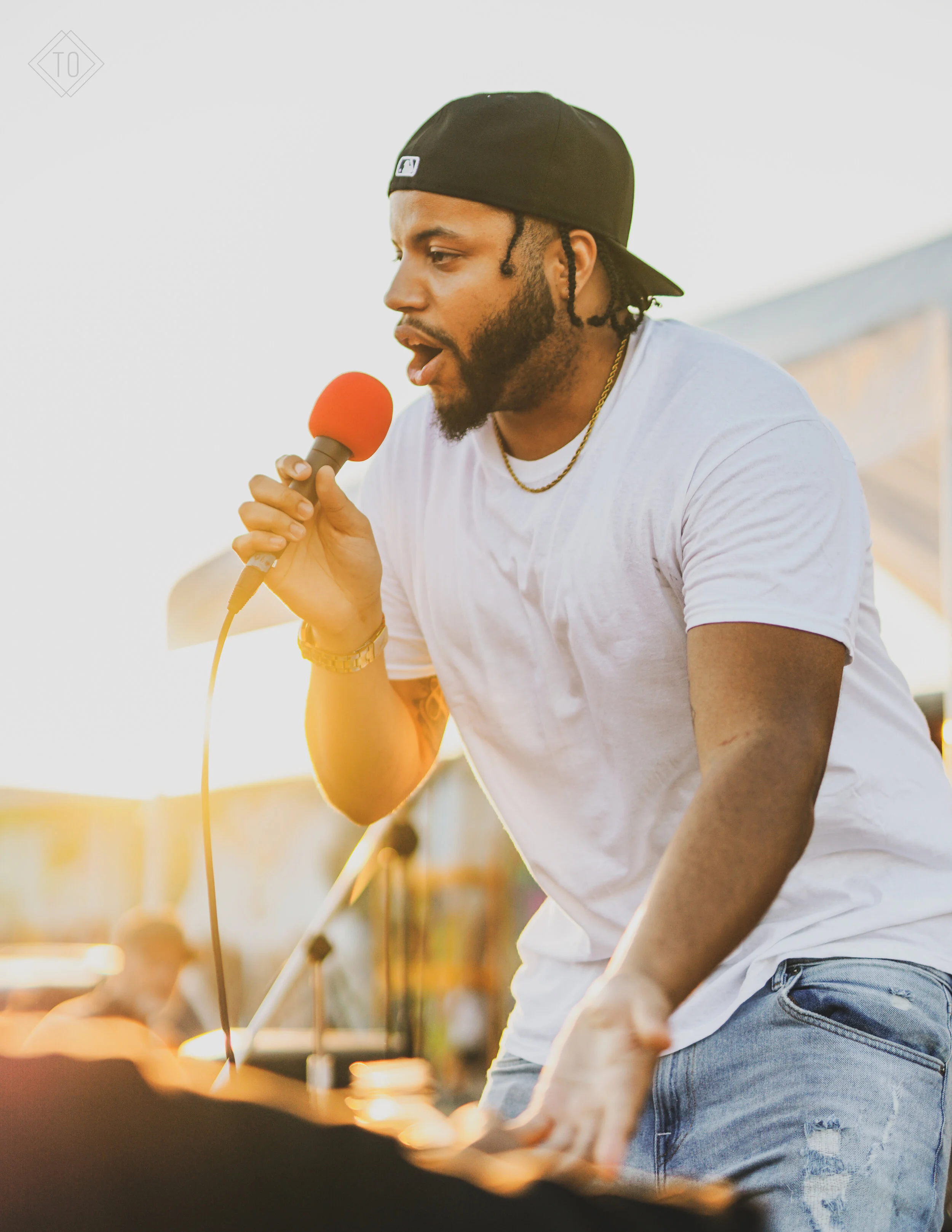 Man singing into a red microphone at an outdoor event during sunset.