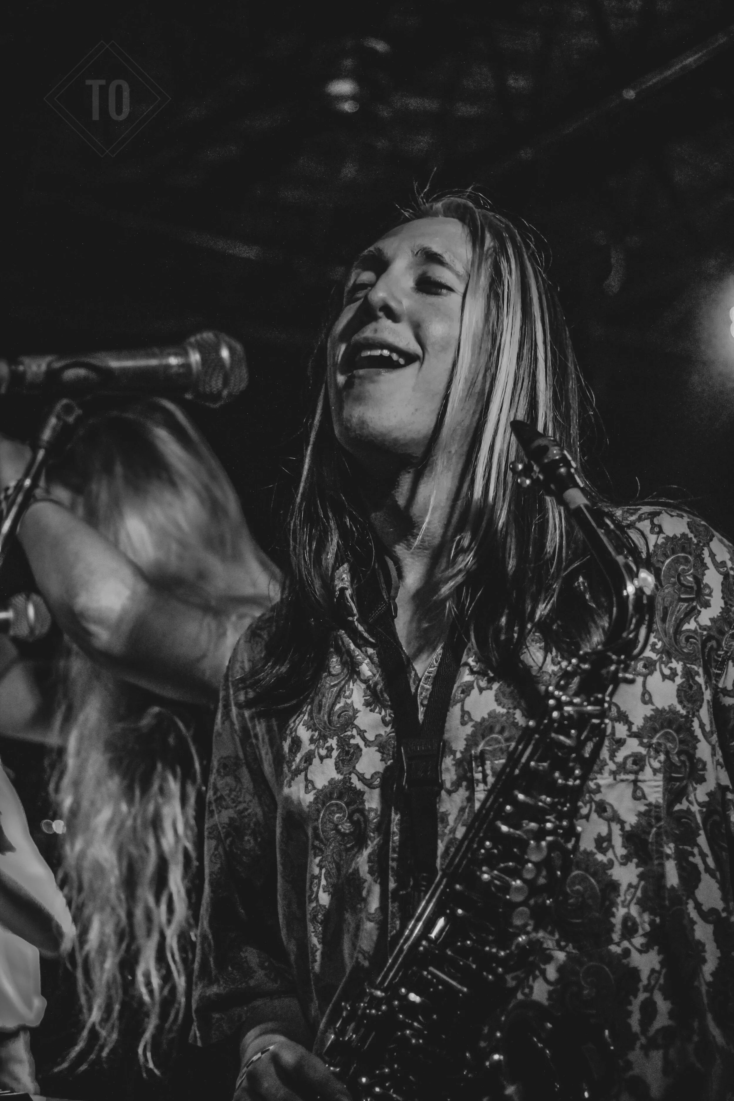 Black and white photo of a woman singing and playing the saxophone on stage, with a microphone in front of her.