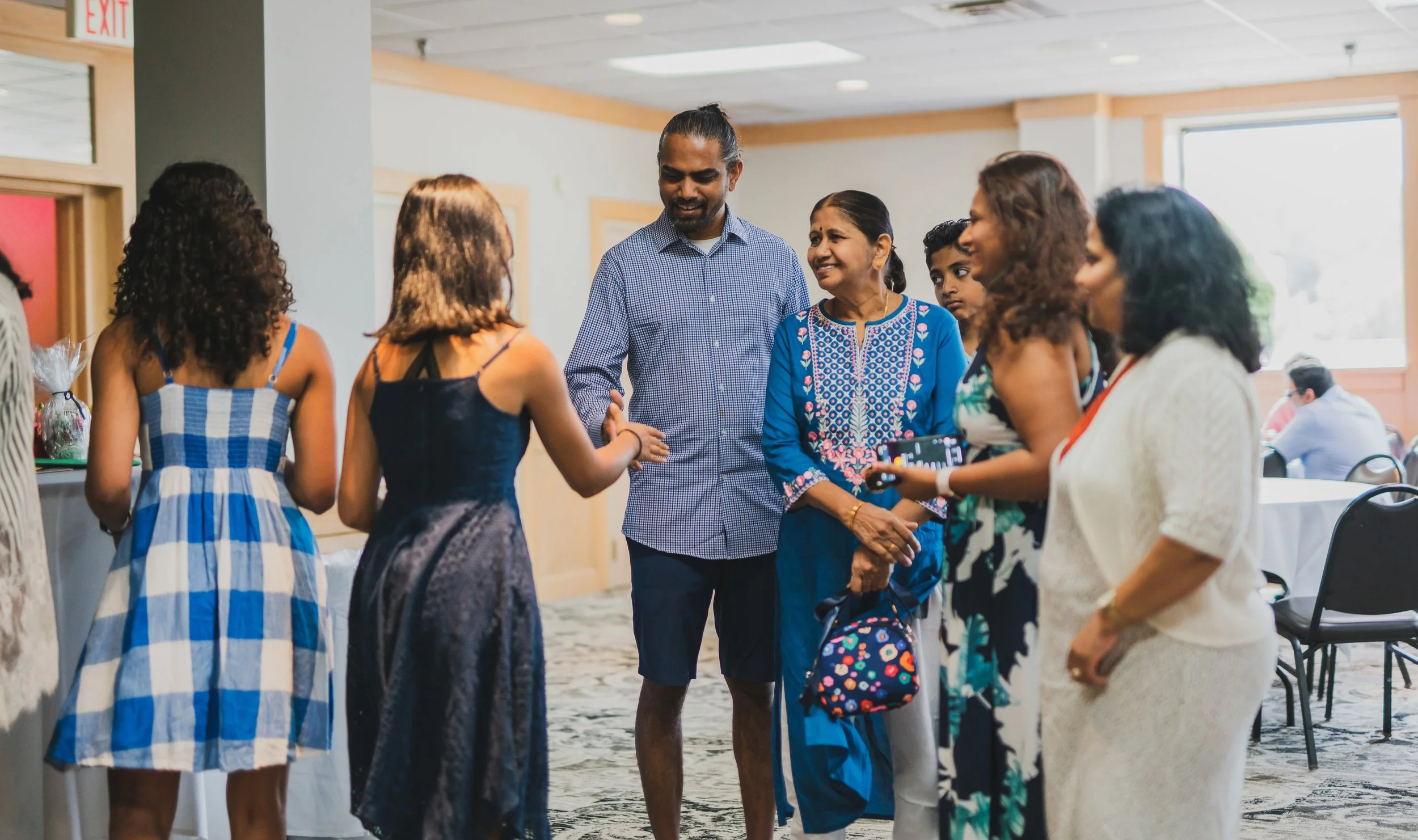 Group of people talking and shaking hands in a room, including adults and children.