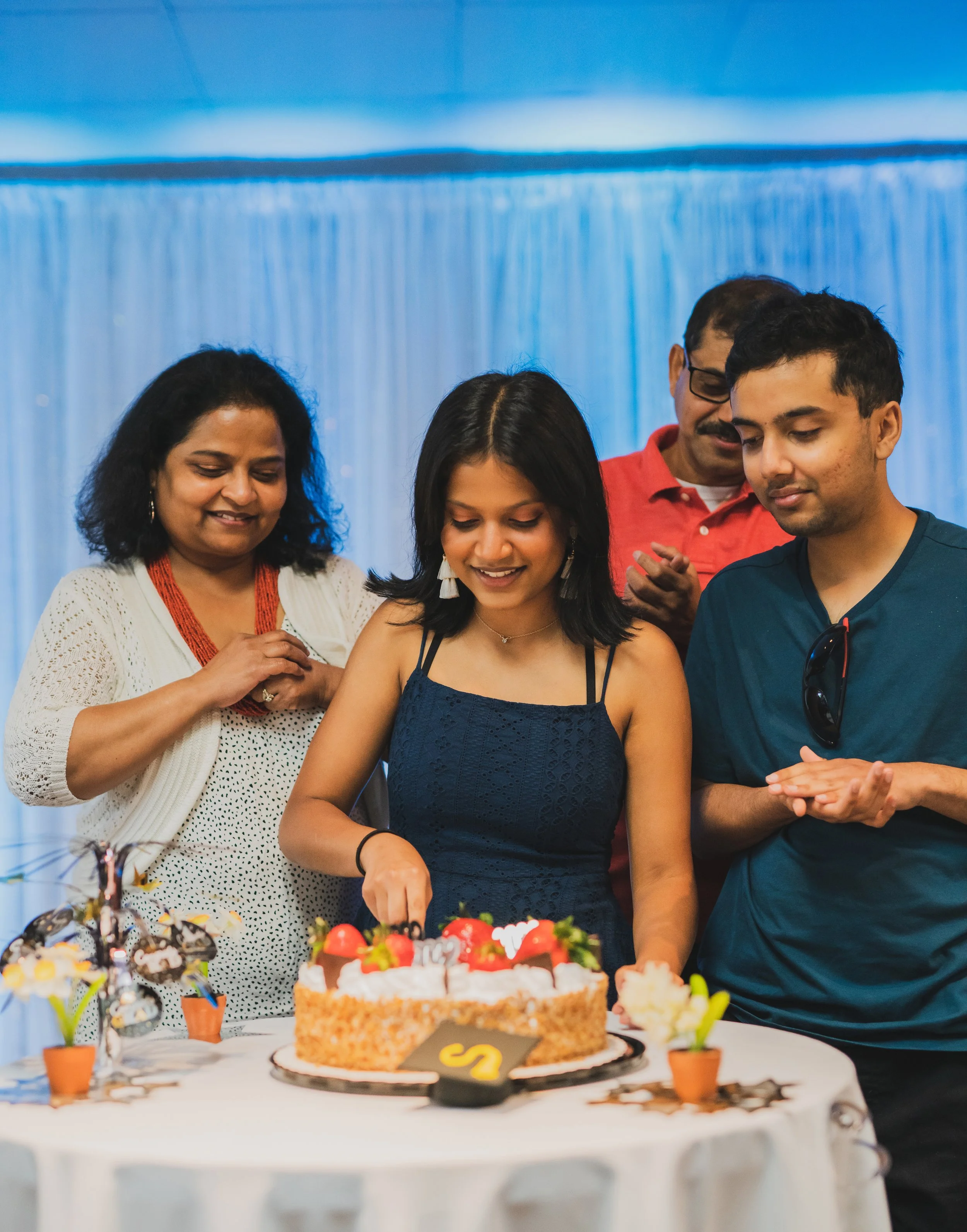A young woman and group of diverse people celebrating a birthday or special occasion with a cake and gifts.