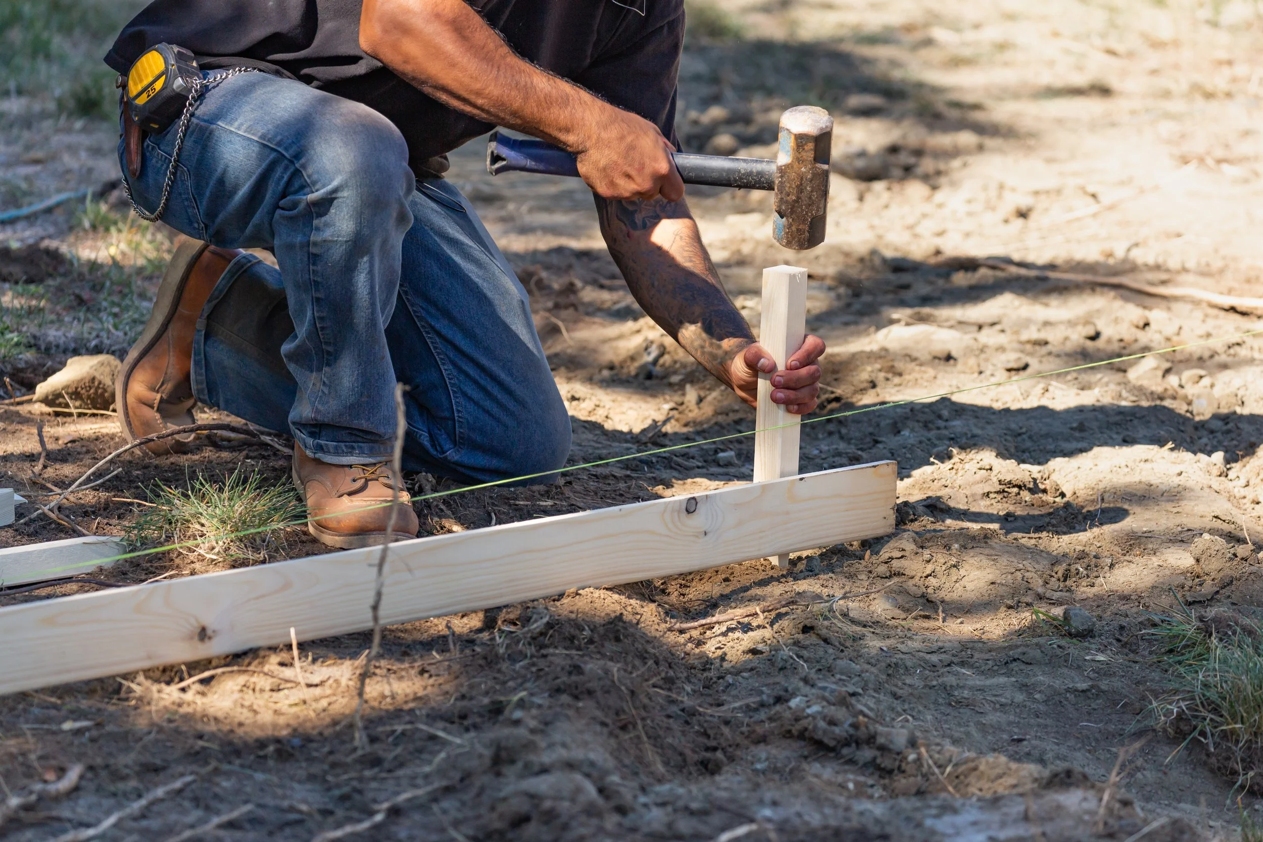 A person kneeling on the ground using a hammer to drive a wooden stake to symbolize community partnership in the Republic of Georgia.