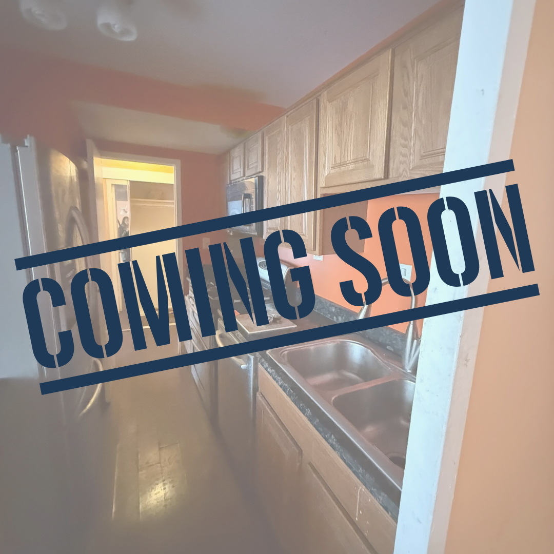 A kitchen with wooden cabinets, a window, and a double sink, overlaid with "Coming Soon" text.