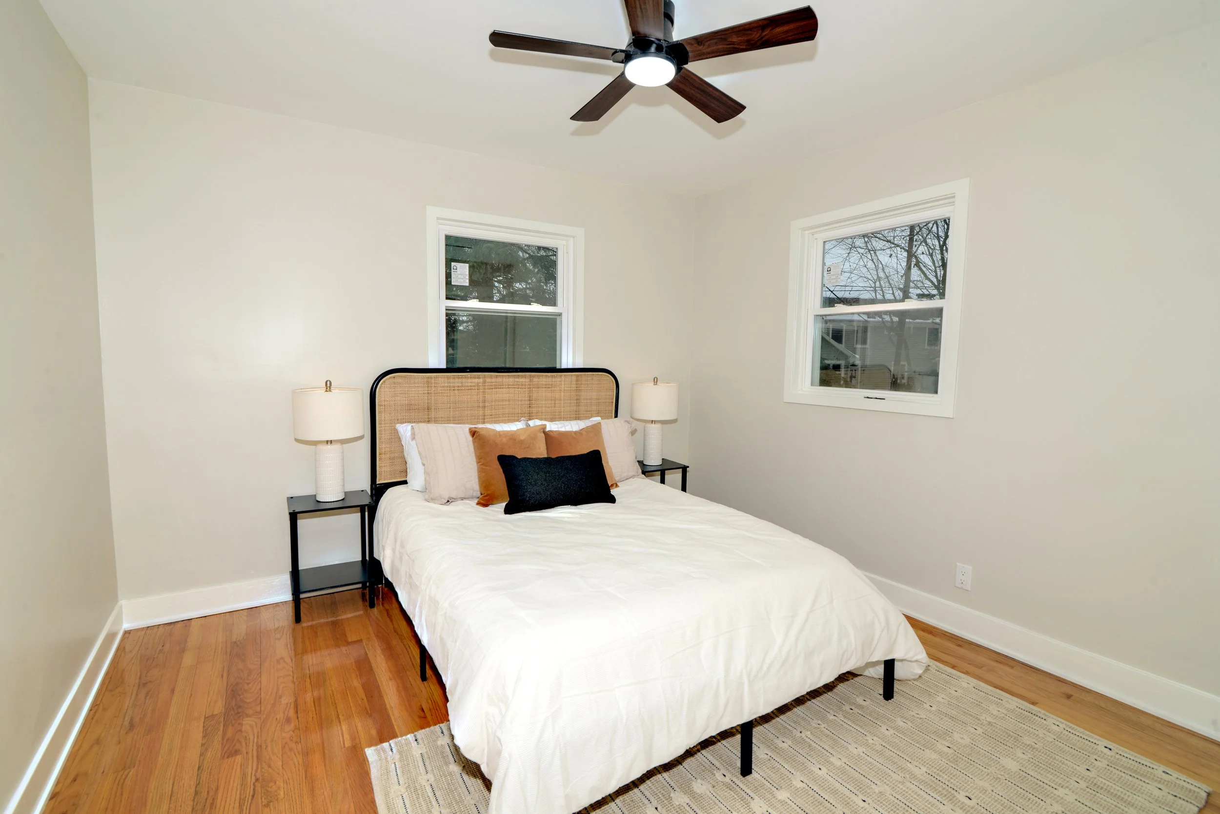 Bedroom decorated clean and crisp, ceiling fan with two windows.jpg
