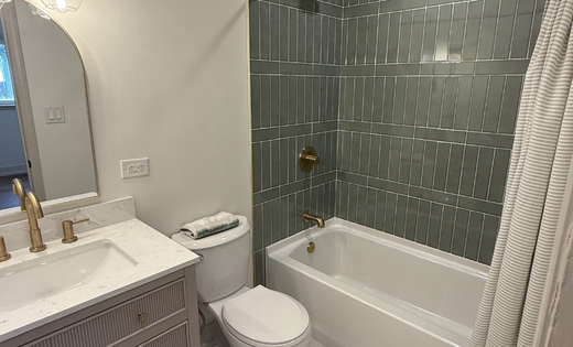 Renovated bathroom with green tile shower, white tub, gold fixtures, and modern vanity