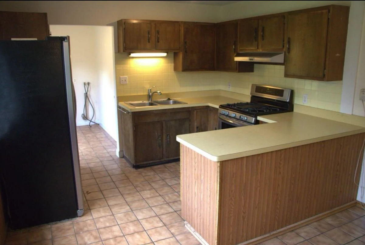 Kitchen with wooden cabinets, black refrigerator, beige countertops, gas stove, and tiled floor.