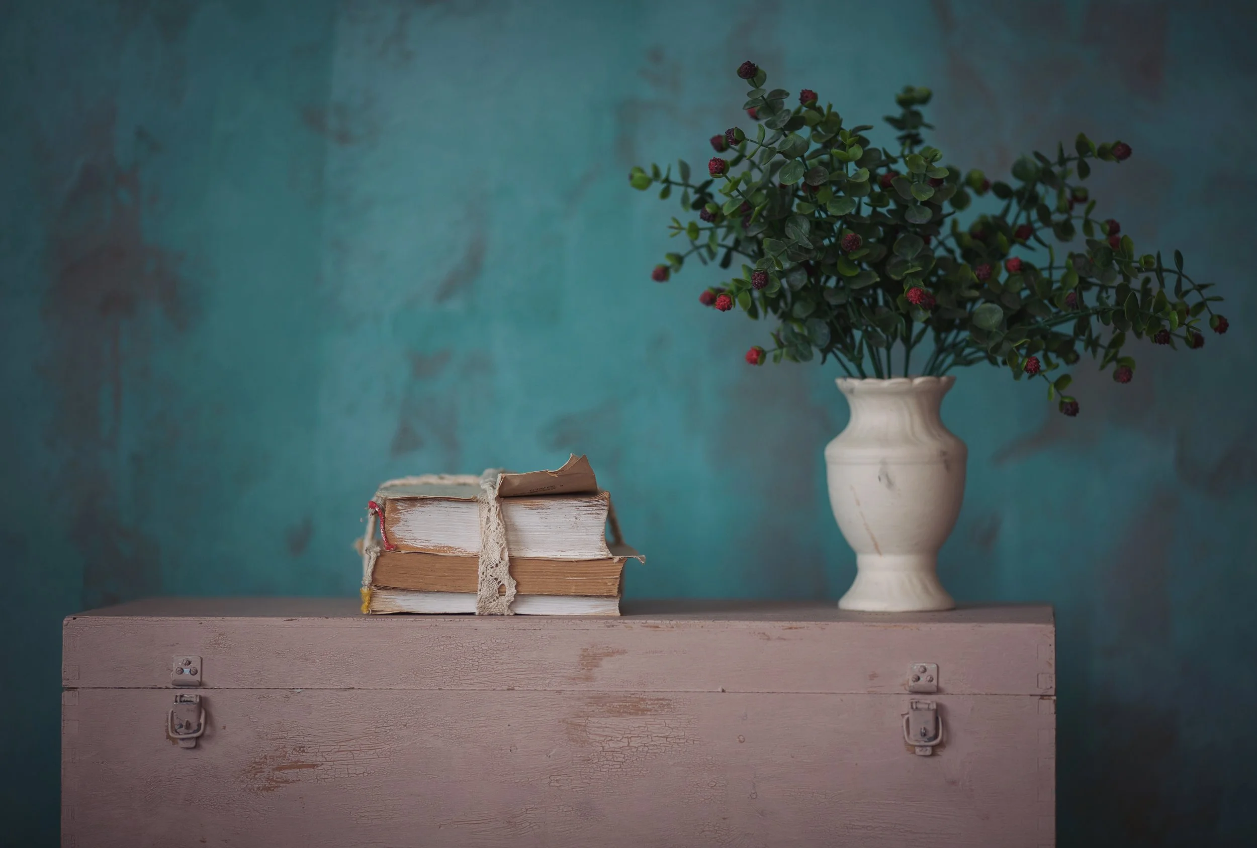 Teal painted interior wall with vintage books, decorative greenery and neutral furnishings.