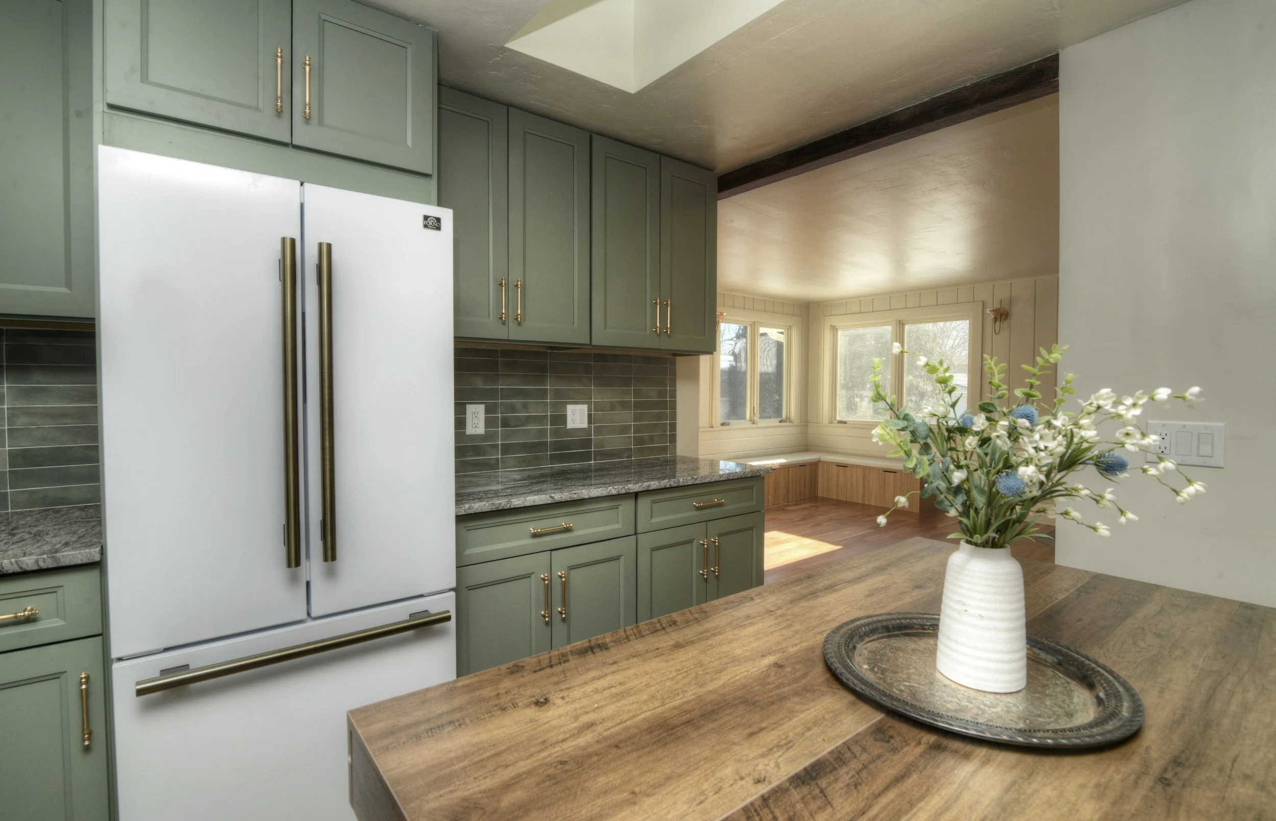 Kitchen with green cabinets, gray countertops, a white refrigerator, and a wooden table with a flower vase.