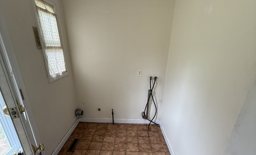 Empty laundry room with tile floor and exposed hookups before renovation