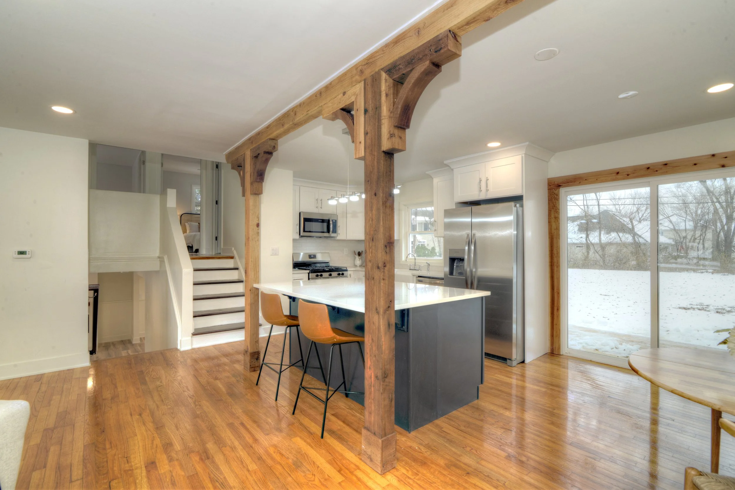 Open kitchen with large island, wood beams, stainless steel appliances, and sliding glass doors