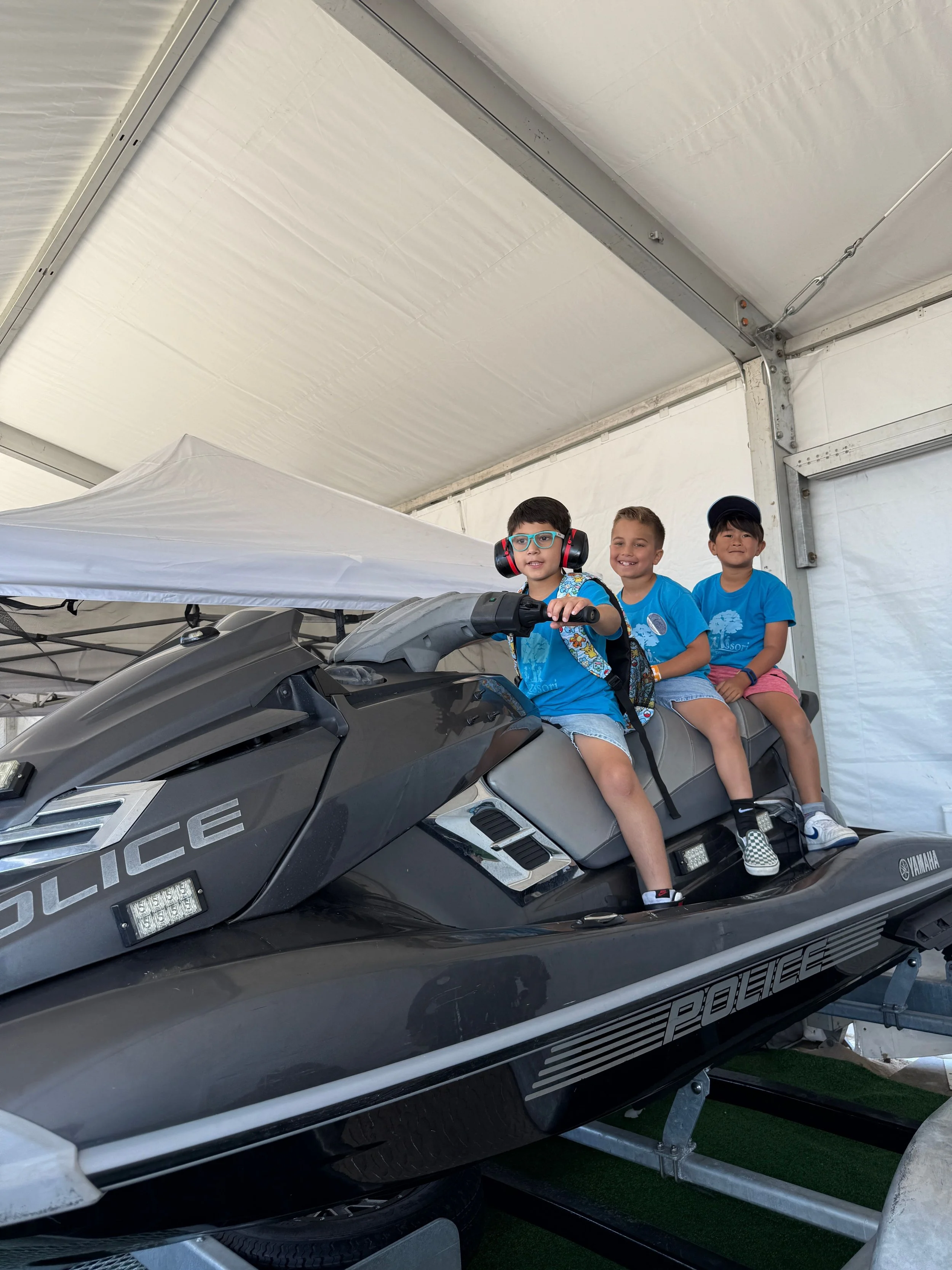 Three children sitting on a police-themed jet ski at an indoor event