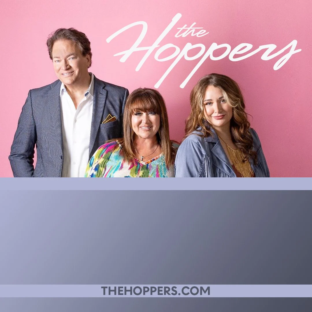 Poster of the TV show 'The Hoppers' featuring three people, two women and one man, standing in front of a pink background with the show's title written in white cursive. The man is on the left wearing a suit, the woman in the middle has red hair and is wearing a colorful top, and the woman on the right has brown curly hair and is wearing a blue jacket.