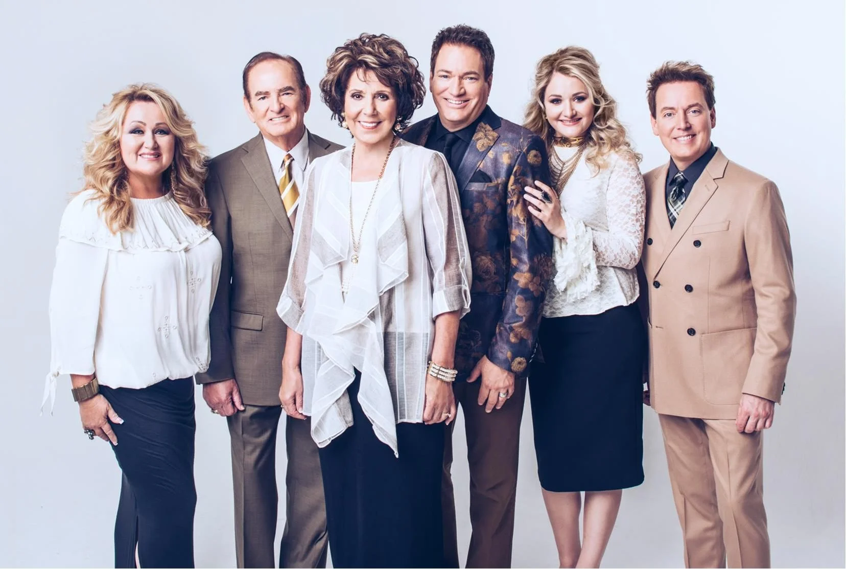 A group of seven professionally dressed people posing together in front of a light background, smiling at the camera.