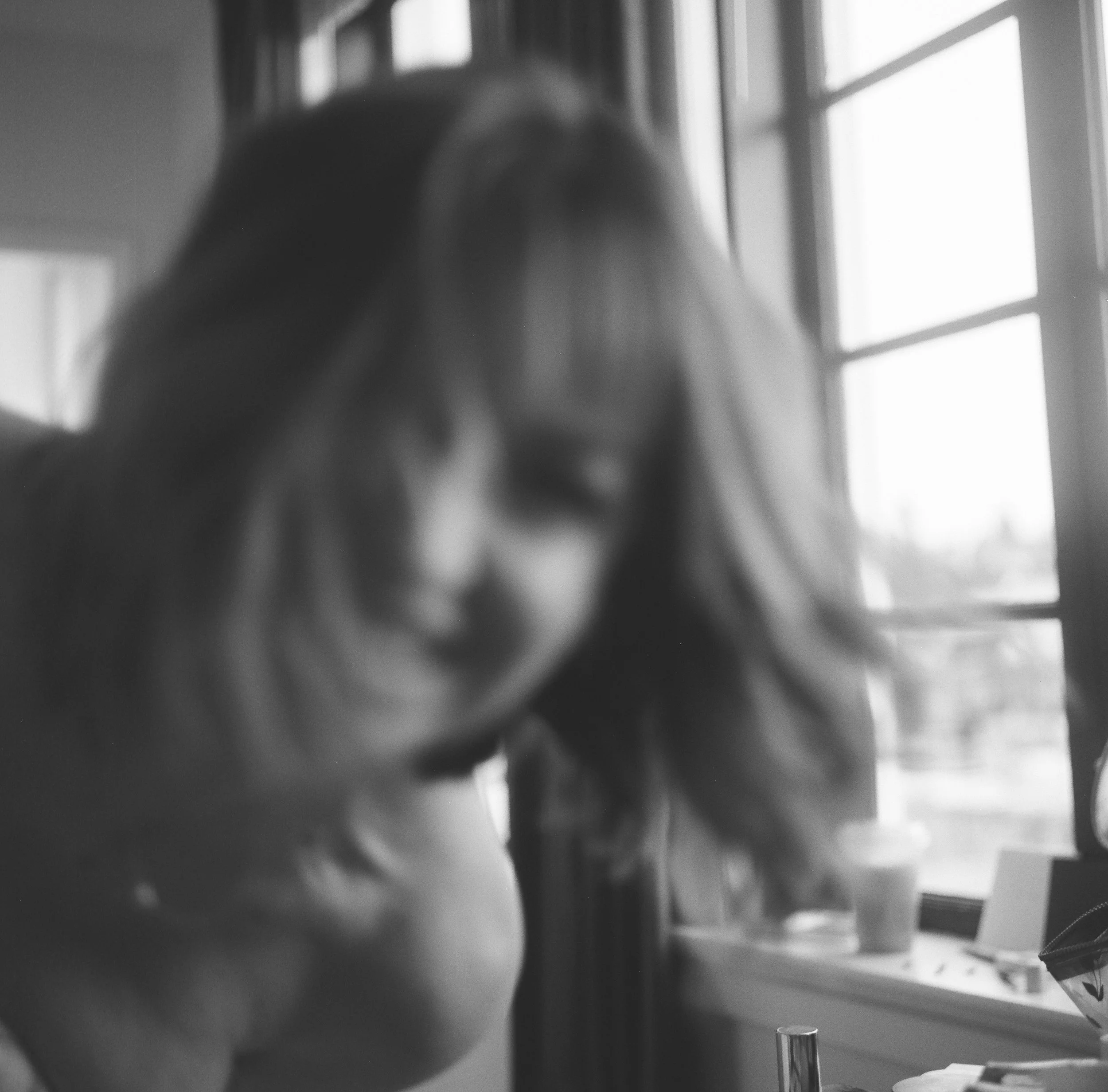 Blurry black-and-white photo of a woman with long hair, smiling near a window with multiple panes.