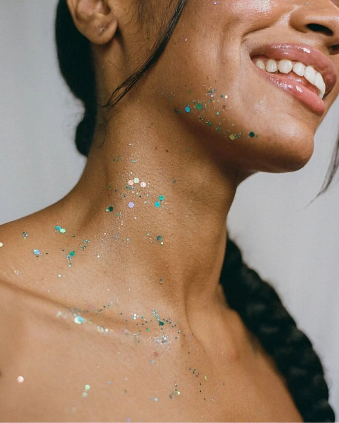 Close-up of a smiling woman with glitter on her neck, shoulder, and cheek.