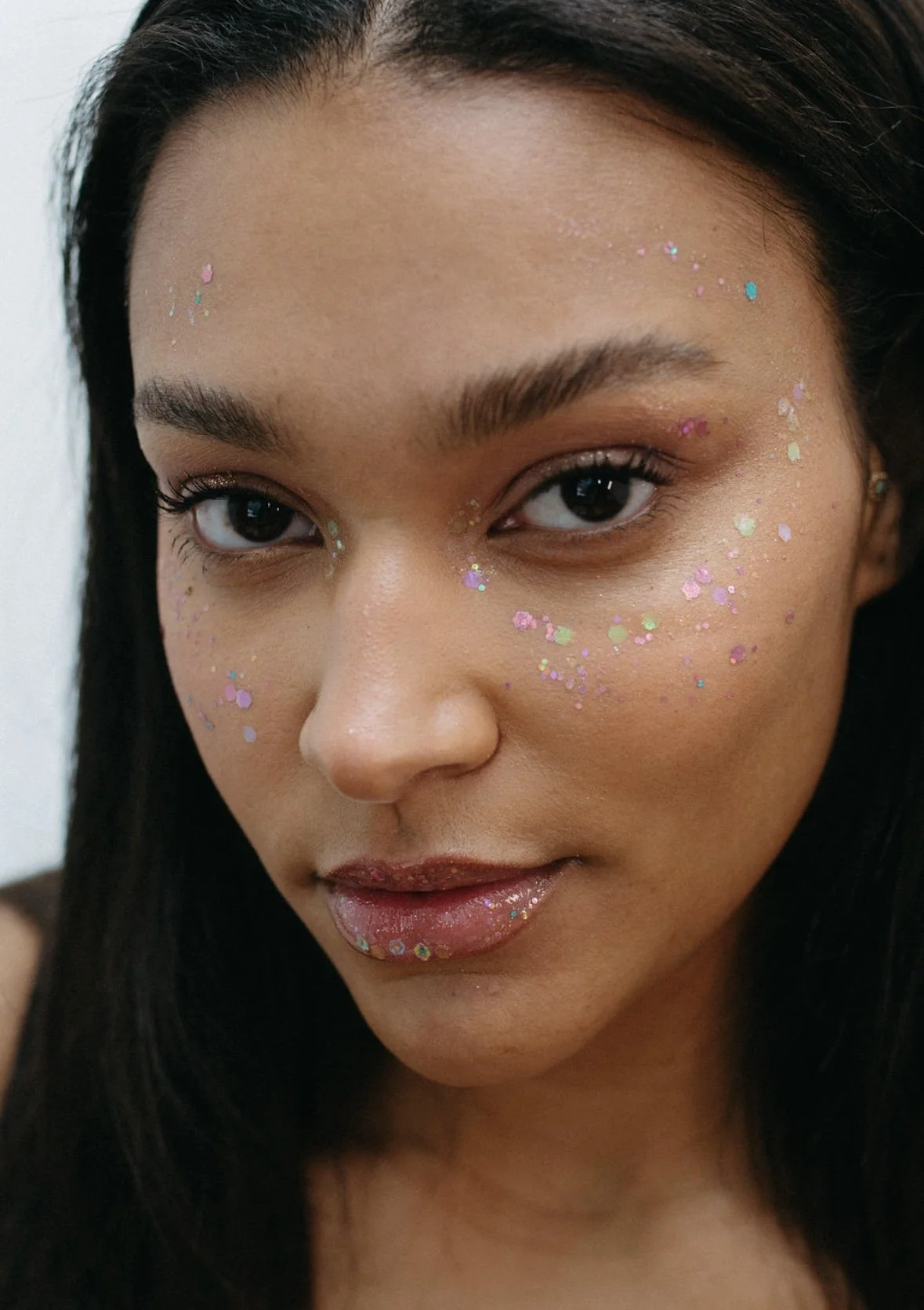 Close-up of a woman with dark hair and glitter makeup, including glitter on her face and lips.