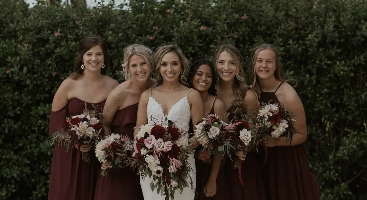 Bride and five bridesmaids holding bouquets outdoors.