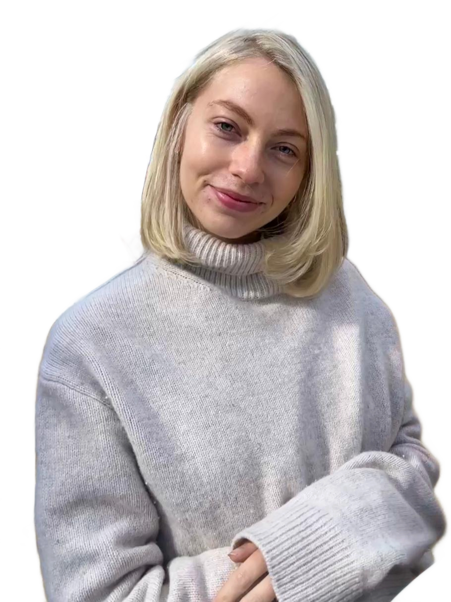 A young woman with blonde hair, smiling softly, wearing a light gray turtleneck sweater, standing against a black background.