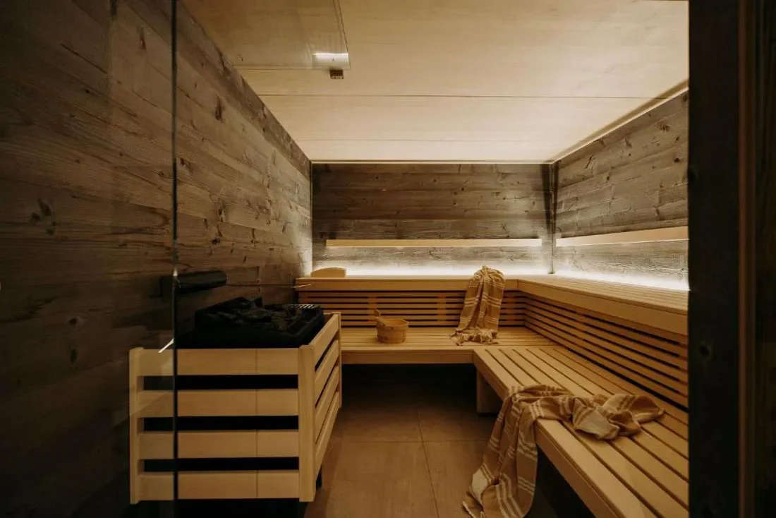 Innenraum einer Sauna mit Holzwänden, Sitzbänken und einem Ofen.