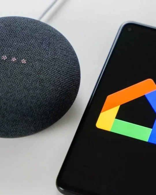 Smart speaker and smartphone displaying Google Photos app on a white surface.