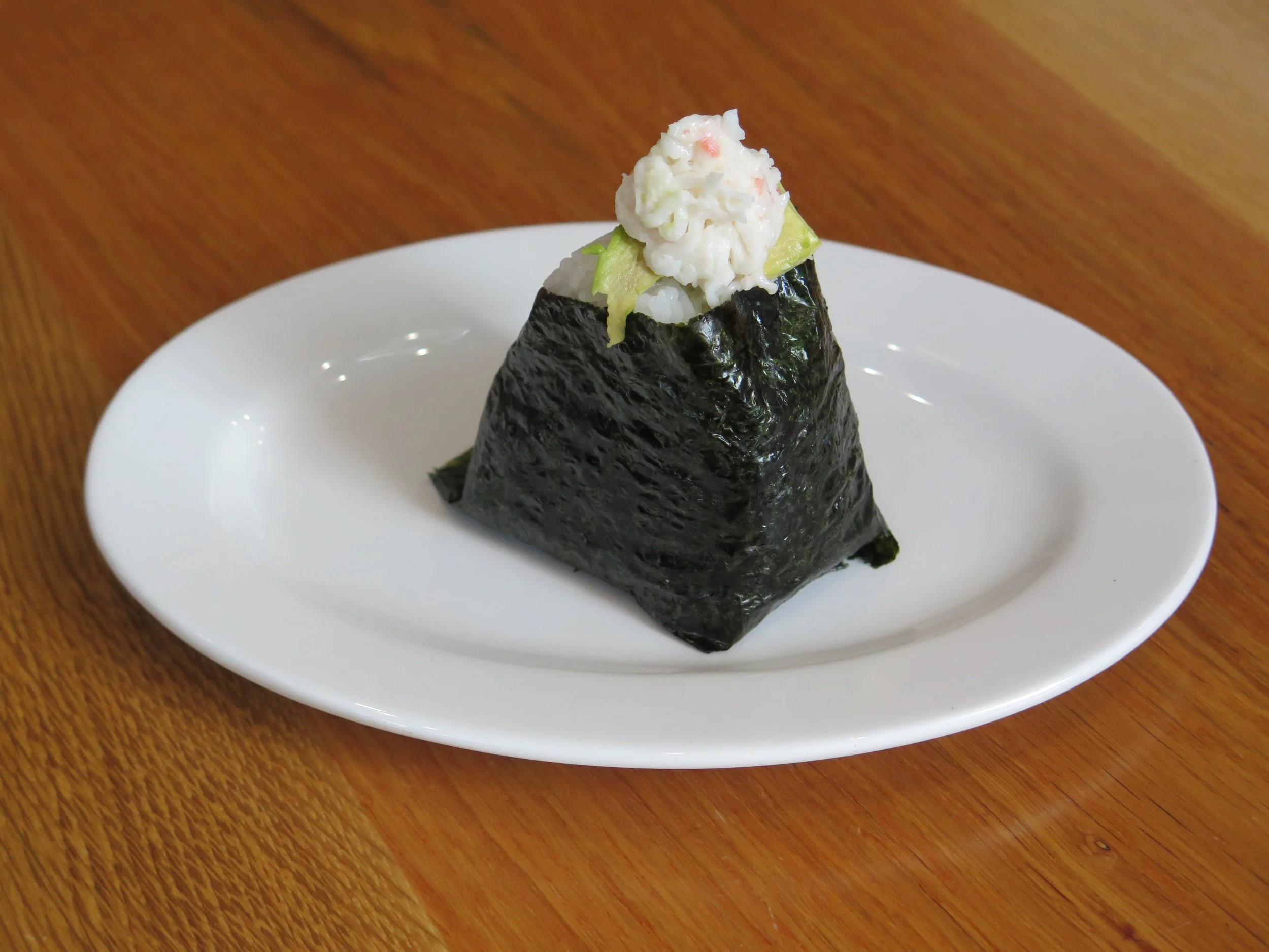 A piece of sushi with a cone shape, wrapped in seaweed, topped with white rice and some creamy topping.