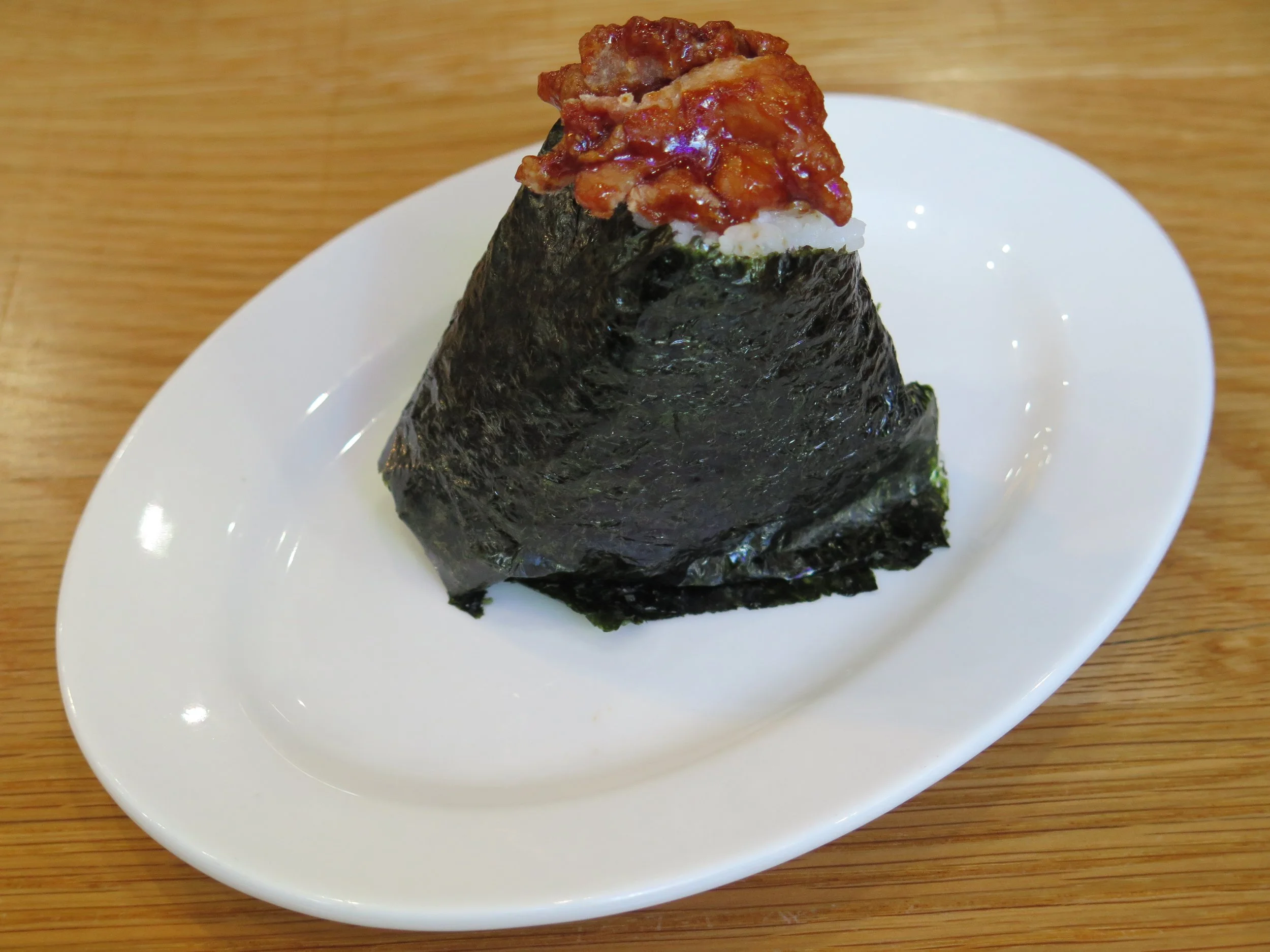 A rice ball wrapped in nori seaweed with a topping of seasoned minced meat on a white oval plate.