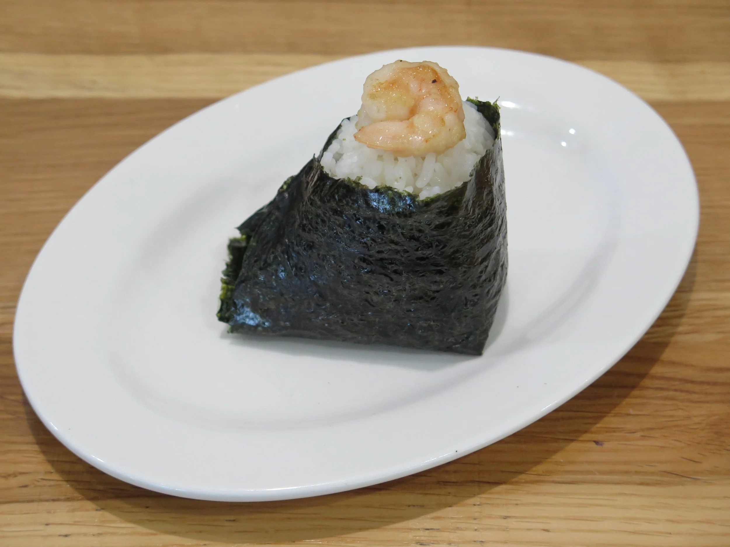 A piece of shrimp nigiri sushi with rice wrapped in seaweed on a white plate
