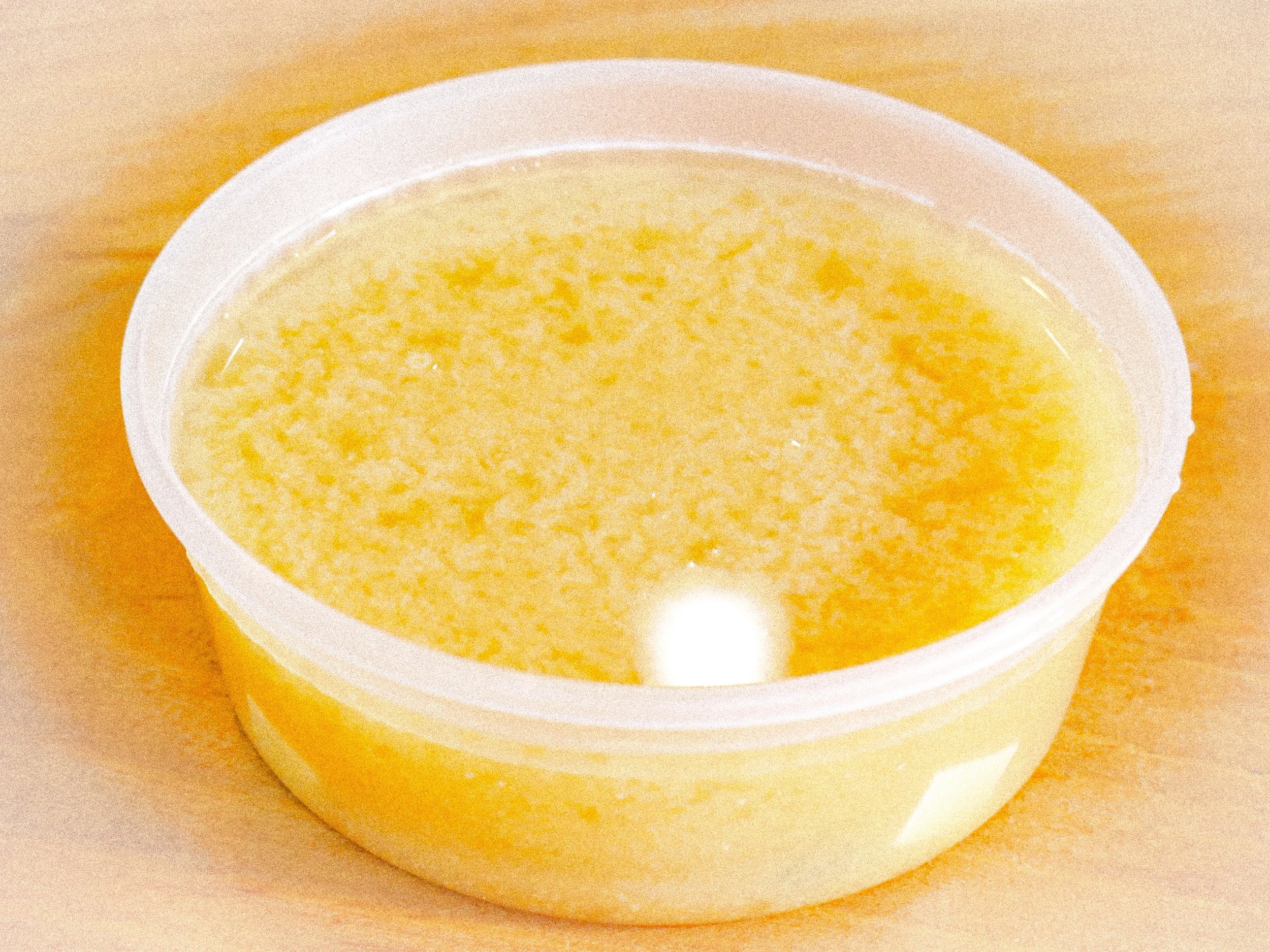 A round, open container filled with a yellow, semi-solid substance, likely butter or margarine, on a wooden surface.