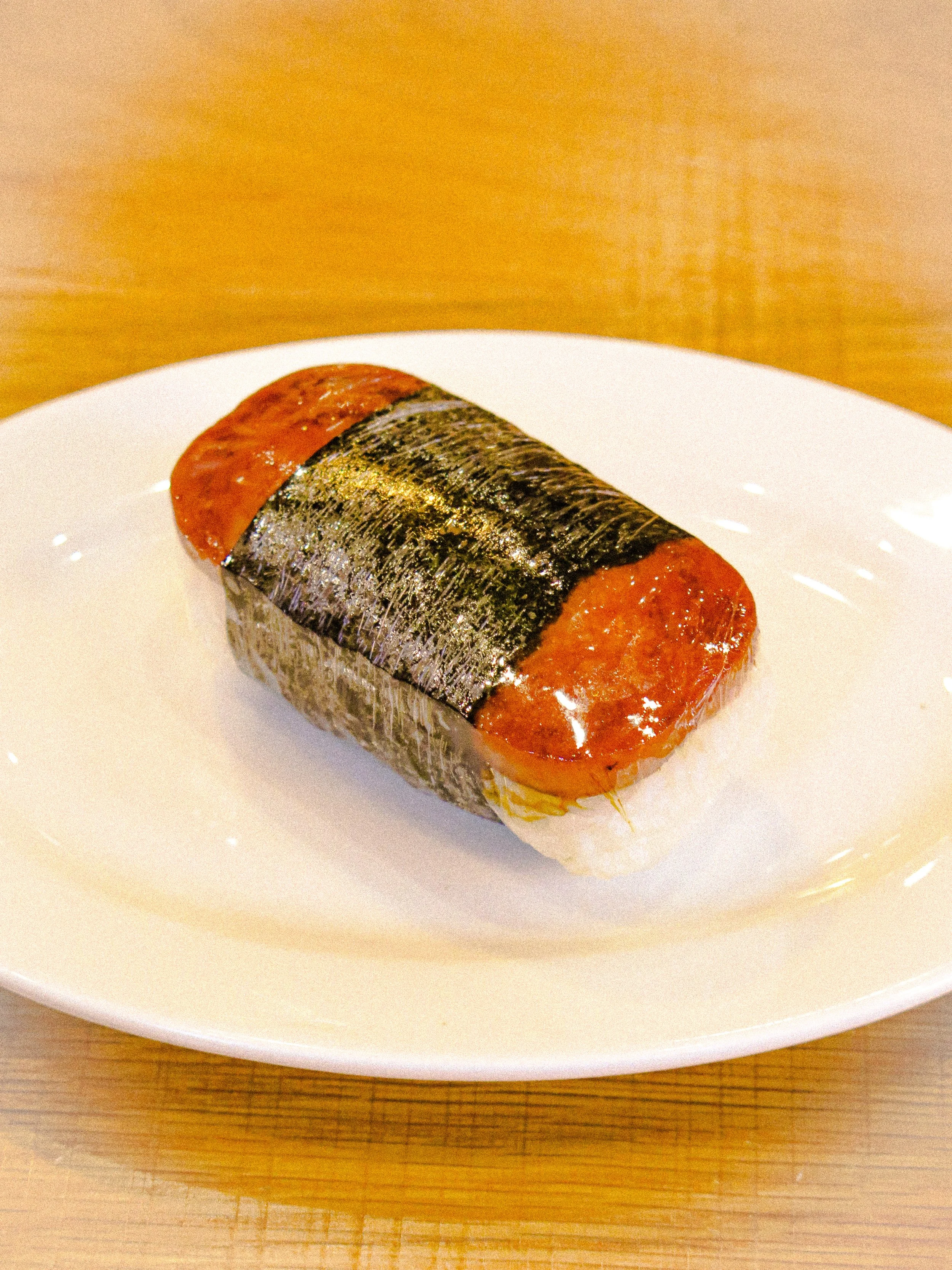 A piece of sushi with a slice of fish and seaweed on top, served on a white plate.