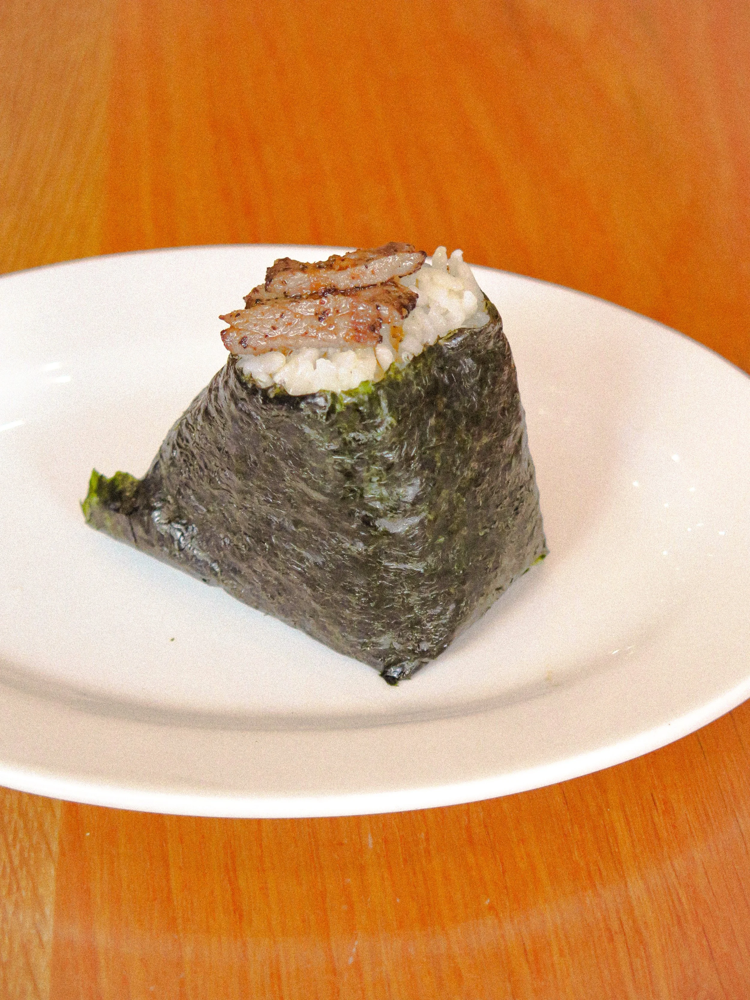 A gunkan-maki sushi with rice, seaweed, and small grilled eel pieces on top, served on a white plate.