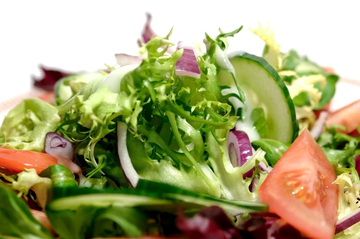 Close-up of a fresh vegetable salad with lettuce, cucumber, tomato, red onion, and dressing